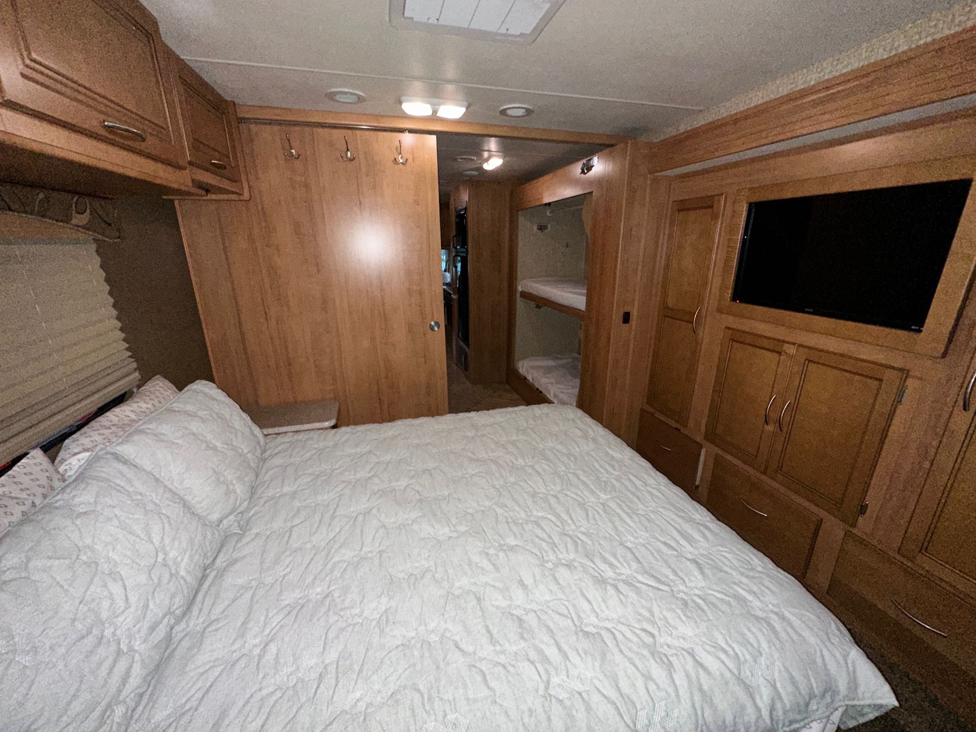 An RV rental interior showing a cozy bedroom with a white queen bed, built-in bunk beds, and wooden cabinetry.. Coachman Miranda 2015