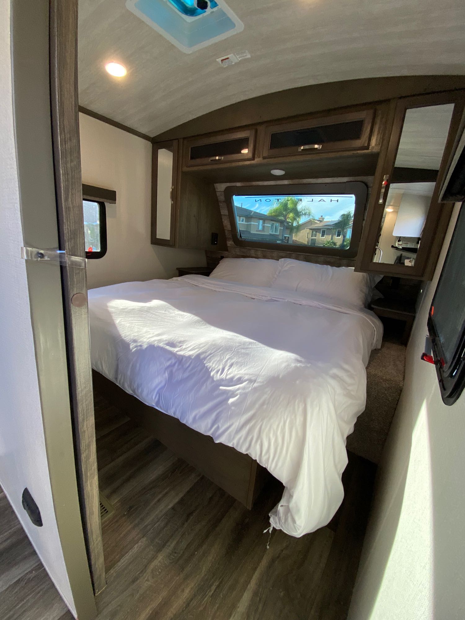 Step into this bright RV rental bedroom, featuring a large bed with white bedding, overhead storage, and natural light.. Keystone RV Cougar 2022