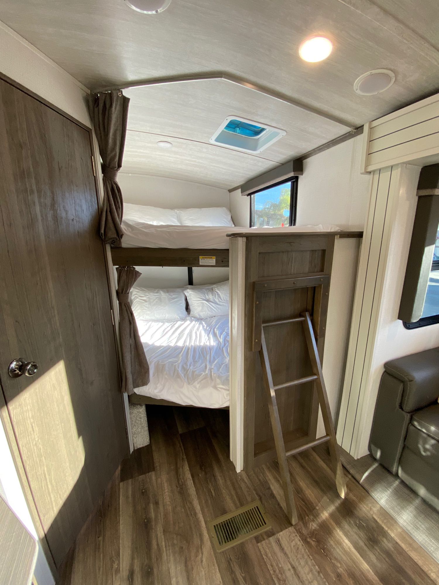 Cozy RV rental interior with bunk beds, white bedding, and a ladder for the top bunk. Wooden door and flooring visible.. Keystone RV Cougar 2022