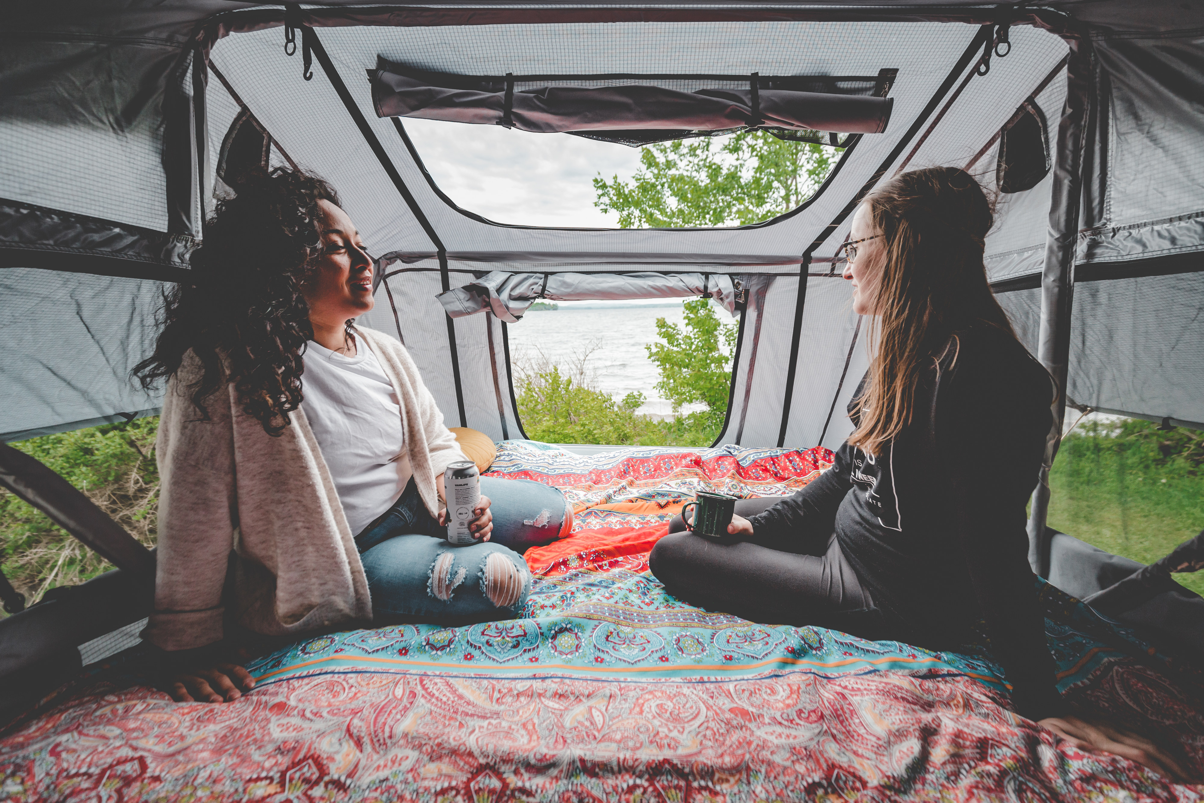 Two friends enjoy lake views from inside their cozy RV rental rooftop tent, a perfect camping escape.. Rooftop Camp S'PA lourd 2024