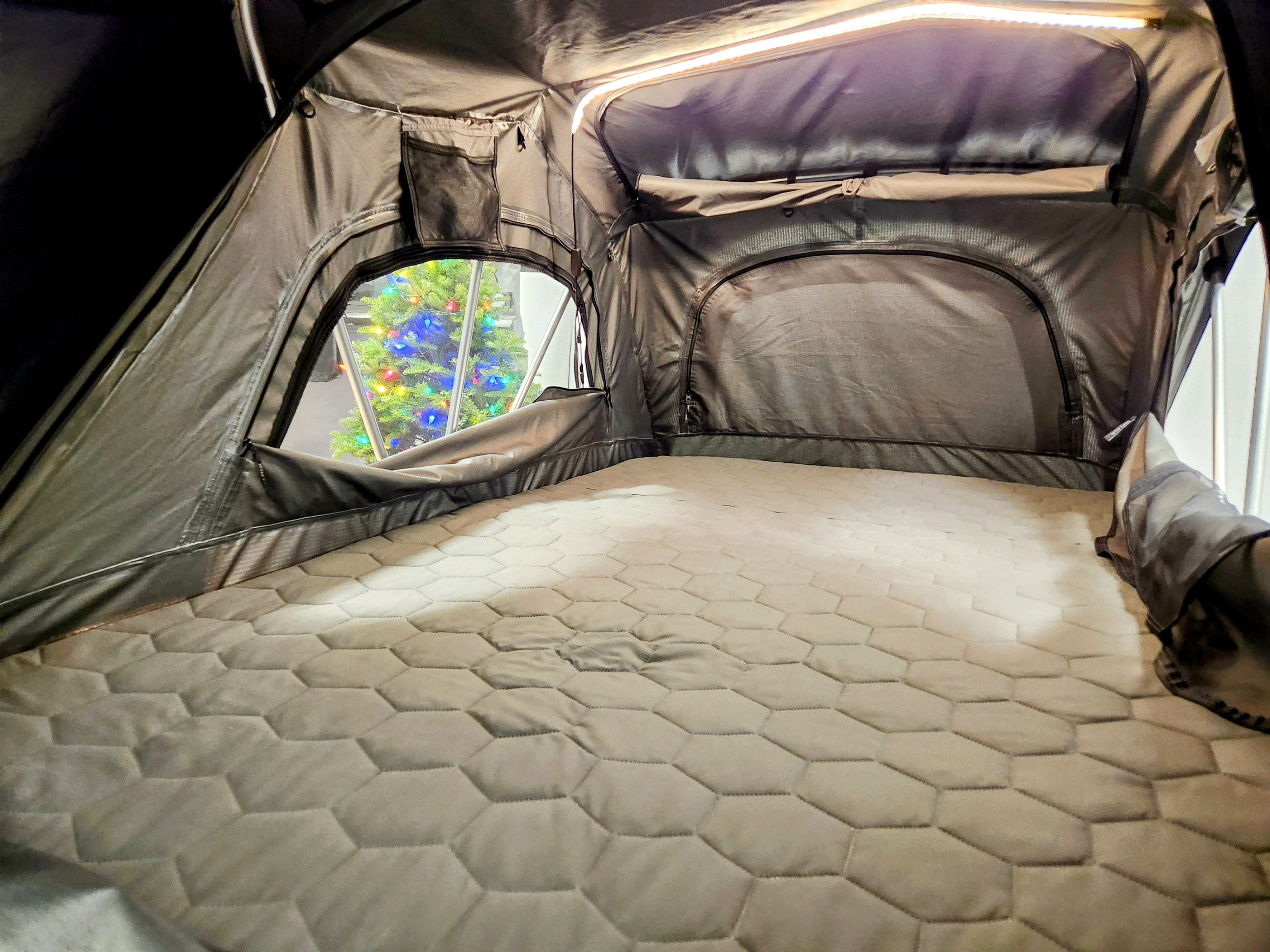 Cozy RV rental interior: hexagonal mattress, built-in light, and a festive Christmas tree seen through the tent window.. Rooftop Camp Vagabond 2024