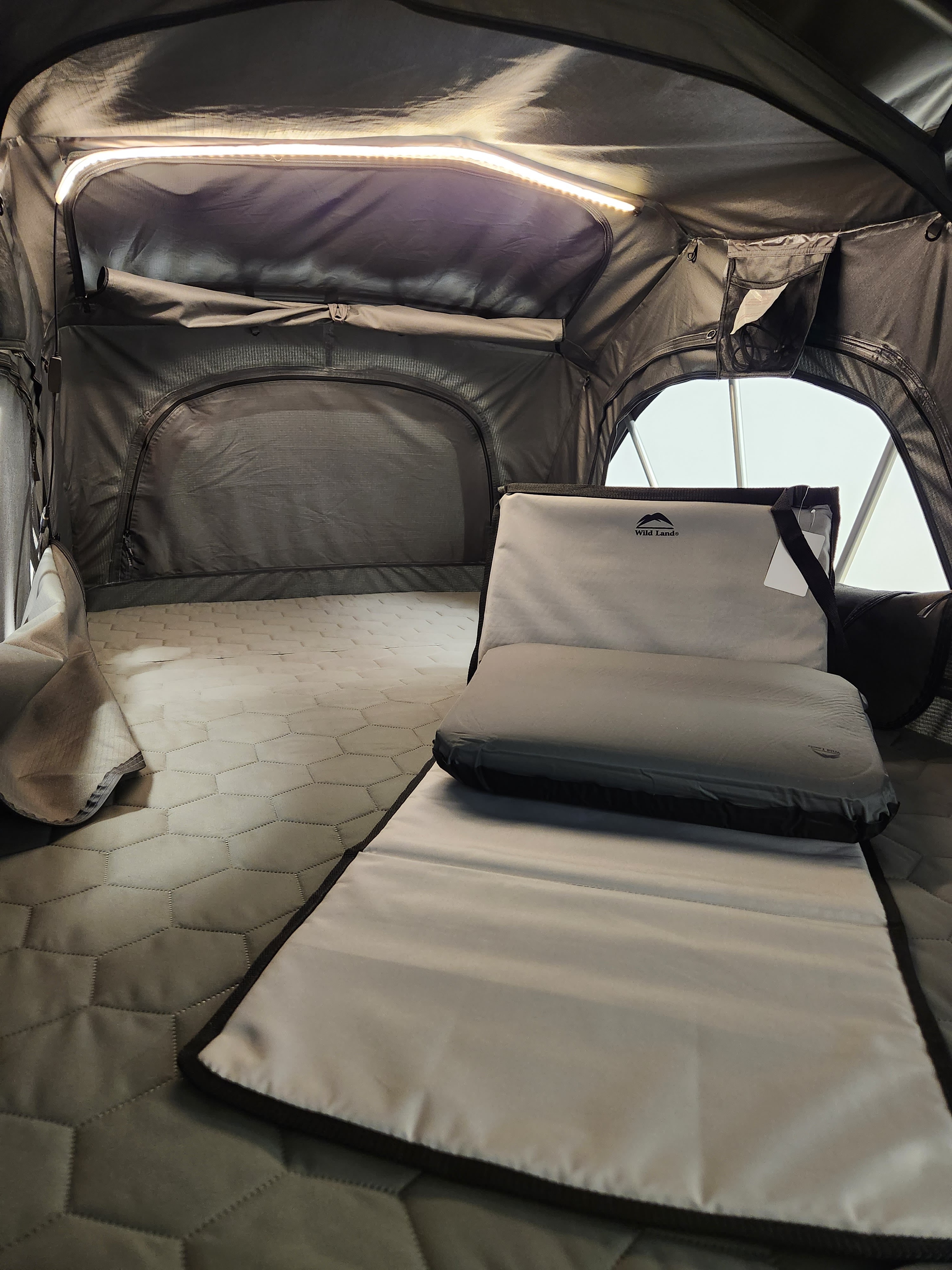 Inside a cozy roof tent, an ideal RV rental sleeping setup. Features a hexagon-quilted mattress, LED light, and a Wild Land cushion.. Rooftop Camp Vagabond 2024