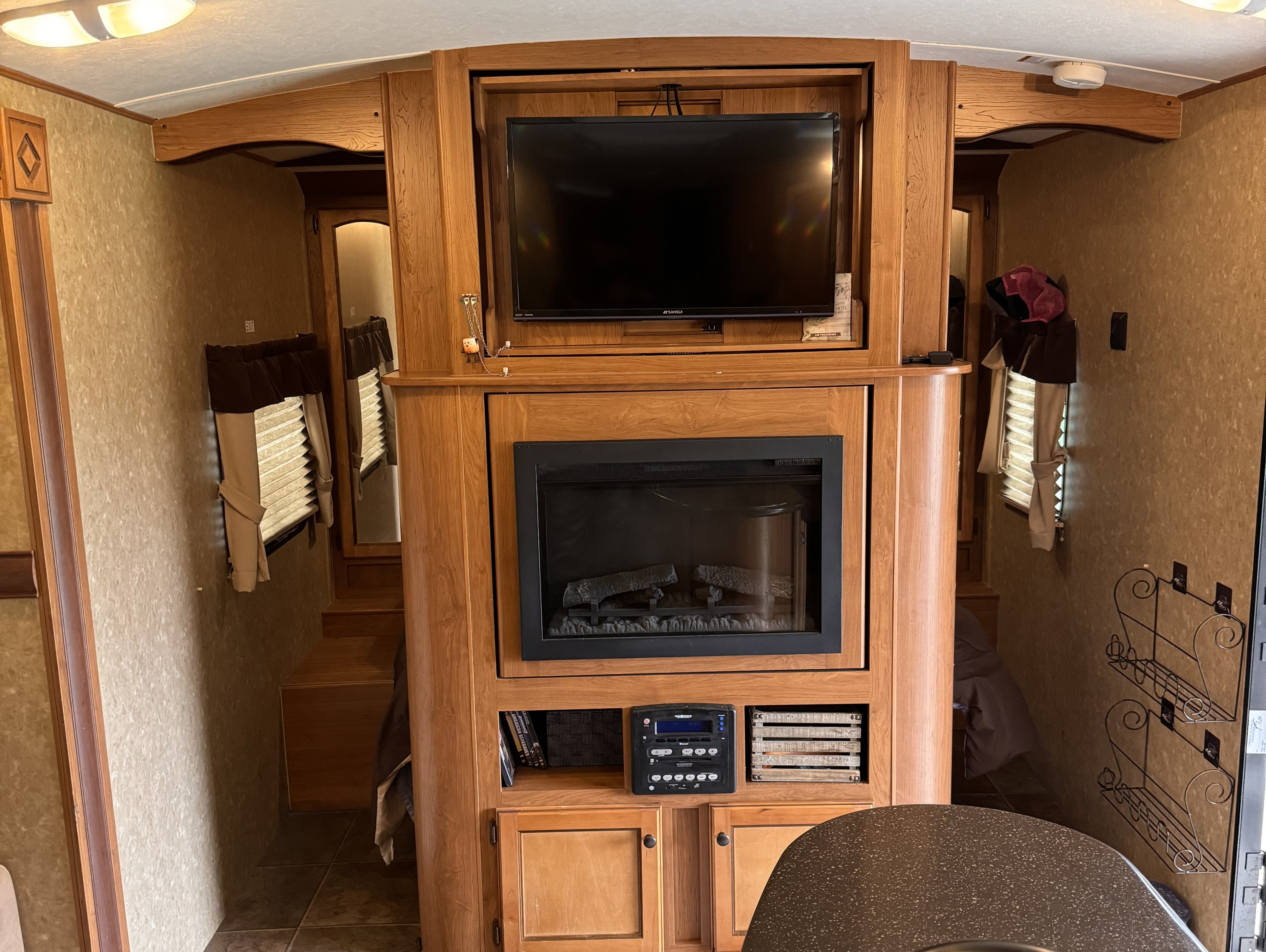 Cozy RV rental interior with a built-in entertainment center featuring a TV and electric fireplace, leading to other areas.. Crossroads Sunset Trail 2014