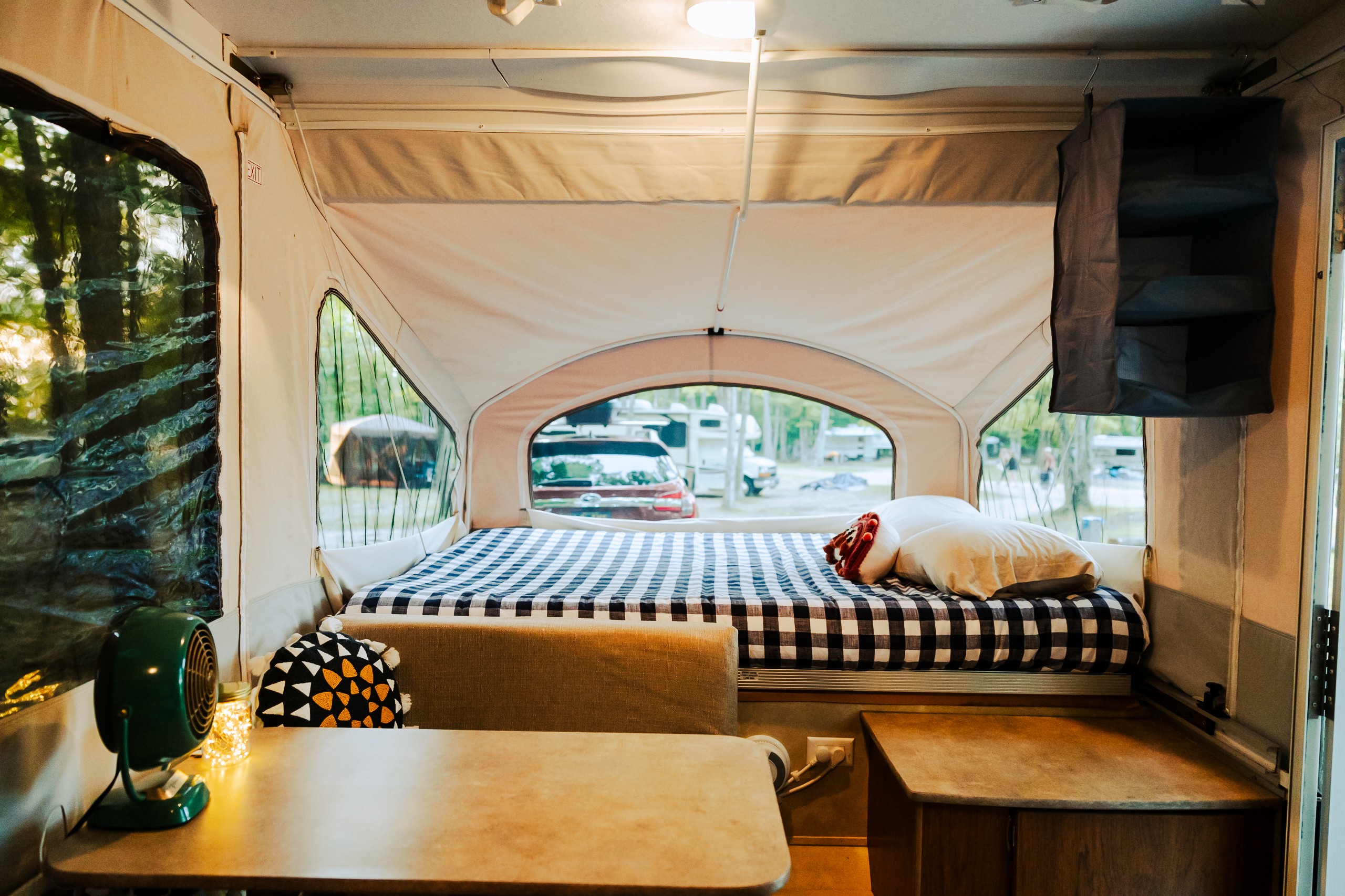 Experience an RV rental! Cozy pop-up camper interior with a checkered bed, table, and window views of a campsite.. Forest River Coachmen 2012