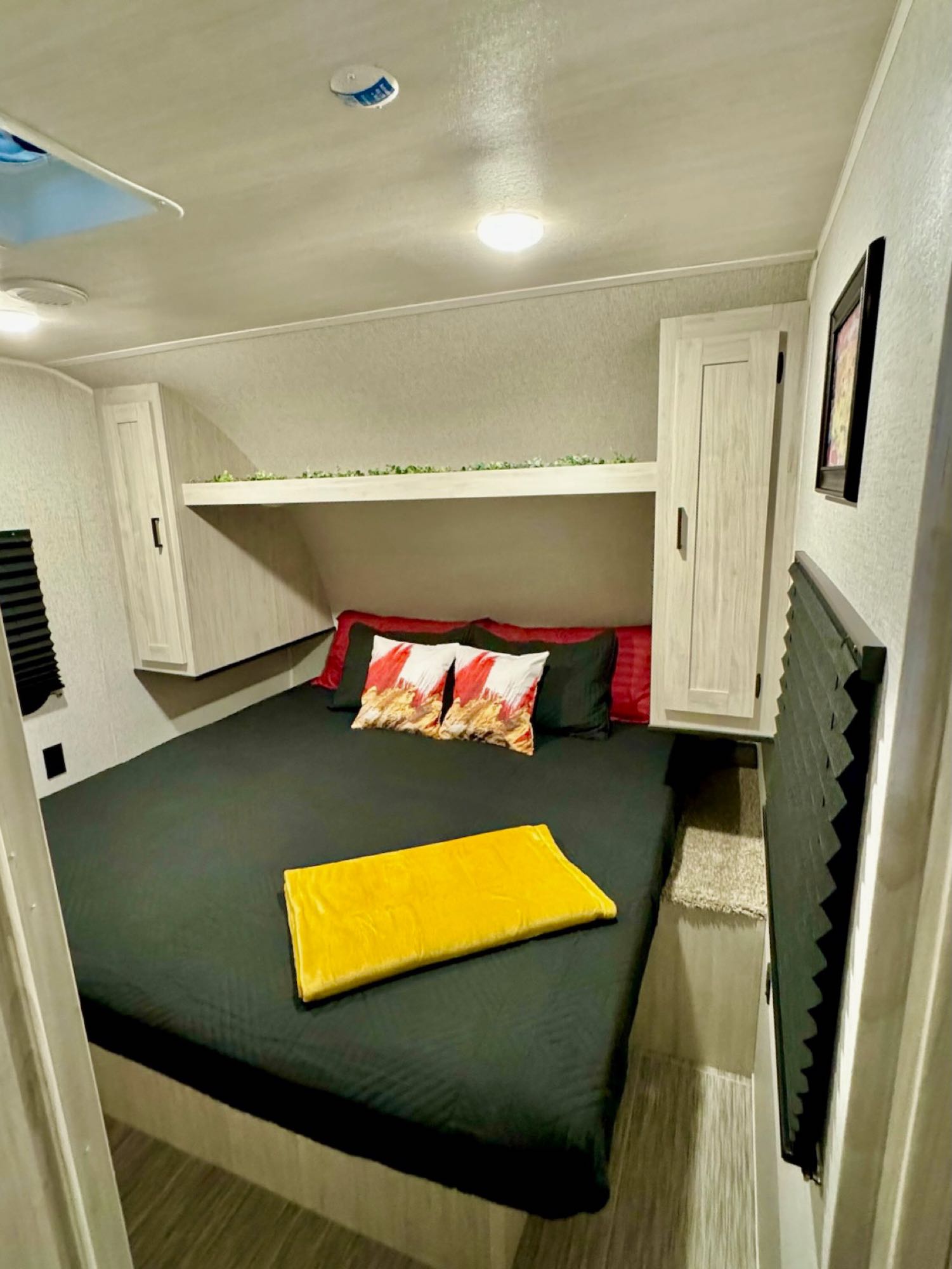 This RV rental bedroom offers a comfortable bed with modern decor, overhead storage, and a shelf. Ideal for travelers.. East to West Silver Lake 2023