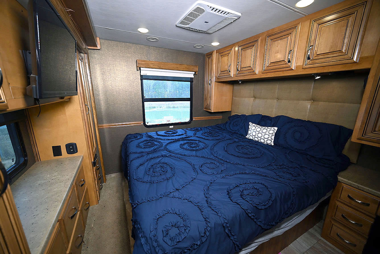 Cozy RV rental bedroom with a large bed, blue ruffled comforter, TV, and overhead cabinets. Ideal for comfortable travel.. Thor Challenger 2016