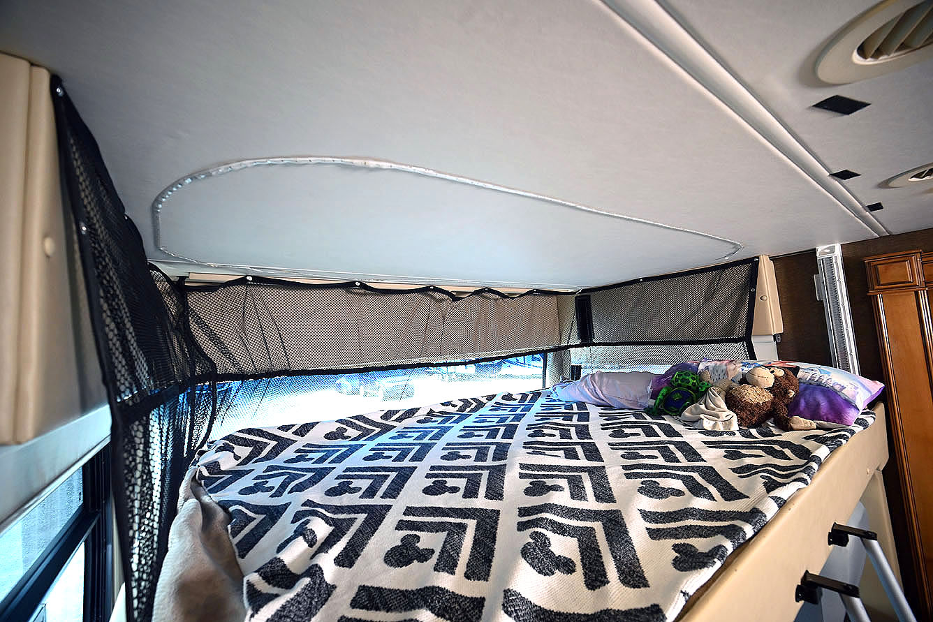 This RV rental bunk bed features a black mesh safety net, cozy blanket, pillows, and stuffed animals for a safe trip.. Thor Challenger 2016
