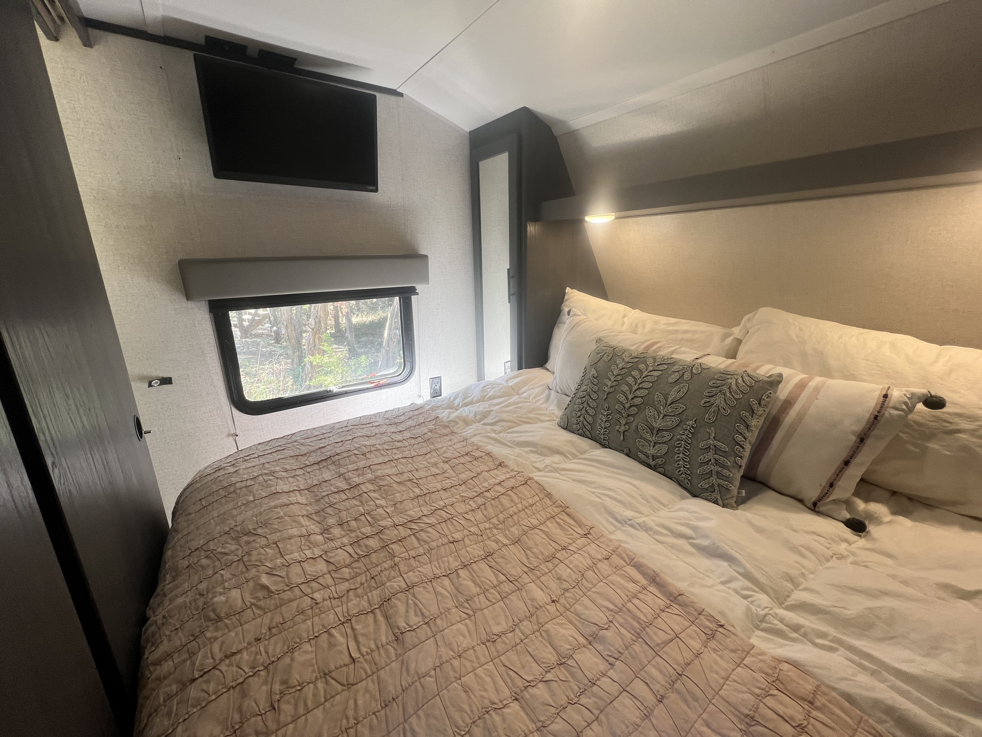Inviting RV rental bedroom with a large bed, decorative pillows, wall-mounted TV, and window to nature.. Dutchmen Aspen Trail 2021