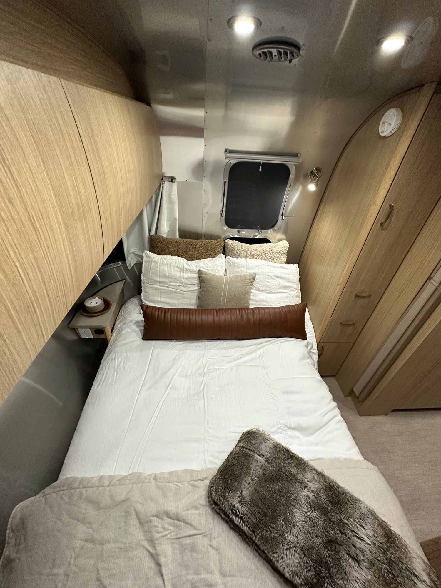 Inside a modern RV rental bedroom featuring a comfy bed, light wood storage, and sleek metallic Airstream walls.. Airstream Flying Cloud 2017