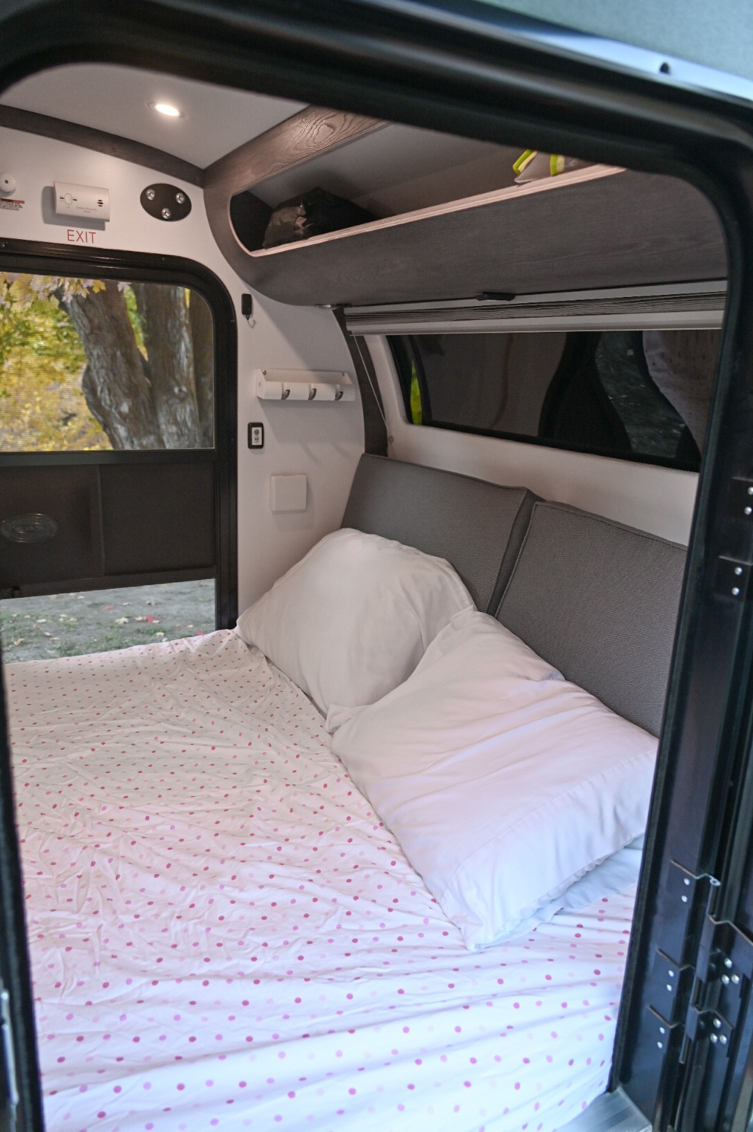RV rental interior: A cozy bed with pink polka-dot sheets, white pillows, and overhead storage awaits adventurers.. bean bean trailer 2021