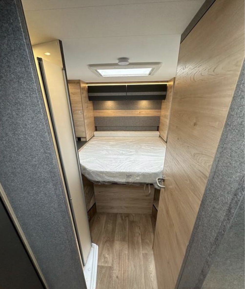 Step into comfort: this RV rental features a cozy bedroom with wood-look flooring, overhead storage, and a bright skylight.. Dethleffs Just Go 2023