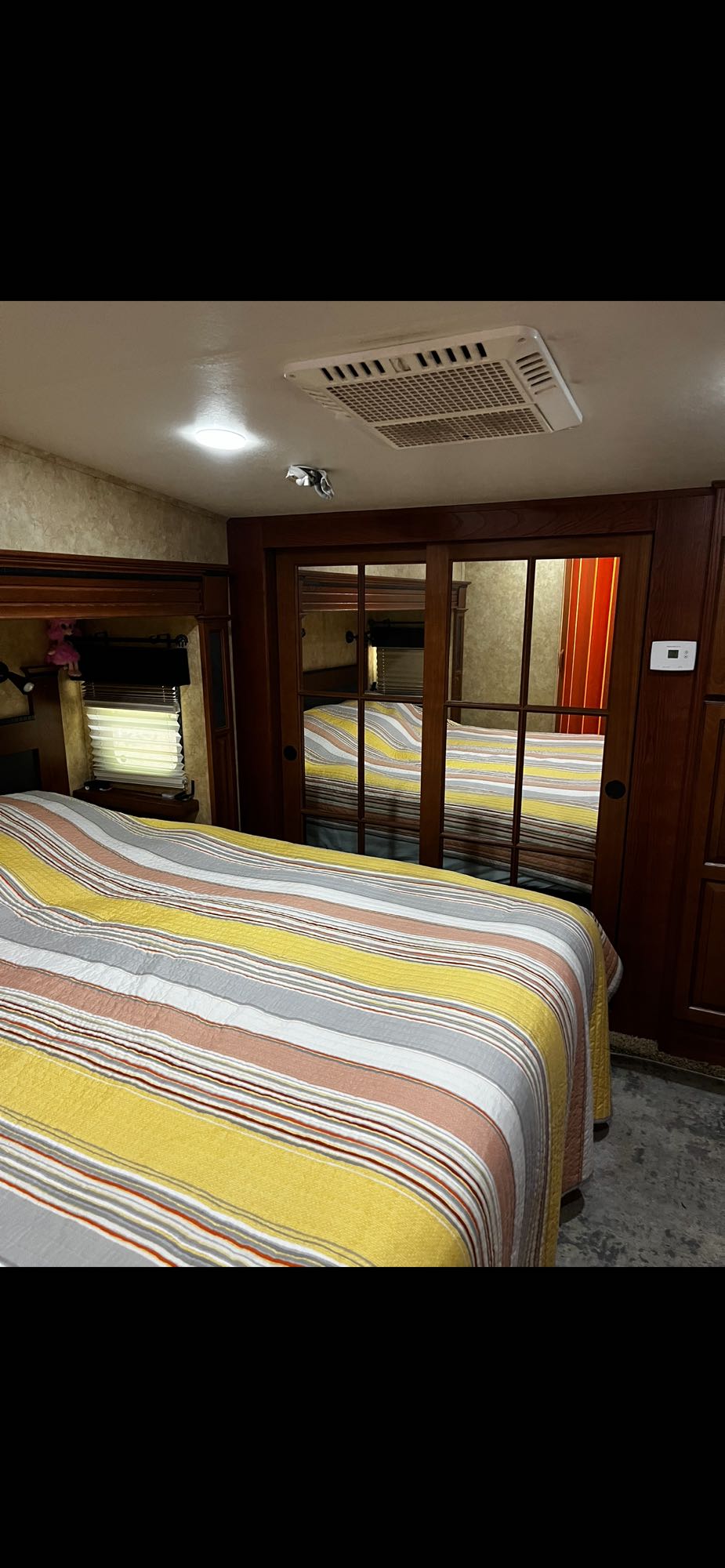 Cozy RV rental bedroom featuring a striped bed, mirrored closet doors, and overhead AC unit for comfort.. Jayco Pinnacle 2011