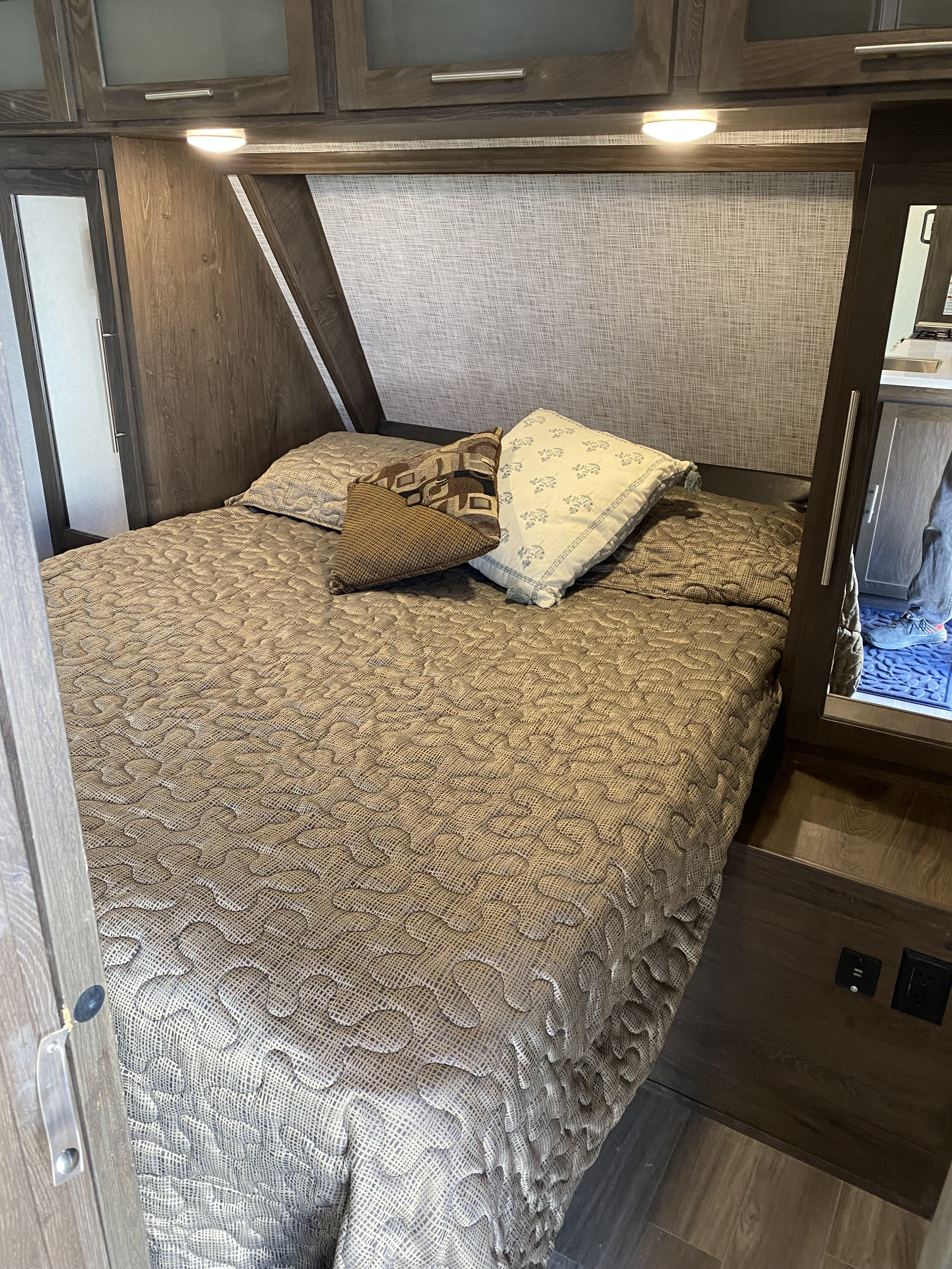 Cozy RV rental bedroom with a patterned bedspread, overhead cabinets, and mirrored wall, offering compact sleeping space.. Forest River Salem Hemisphere GLX 2019