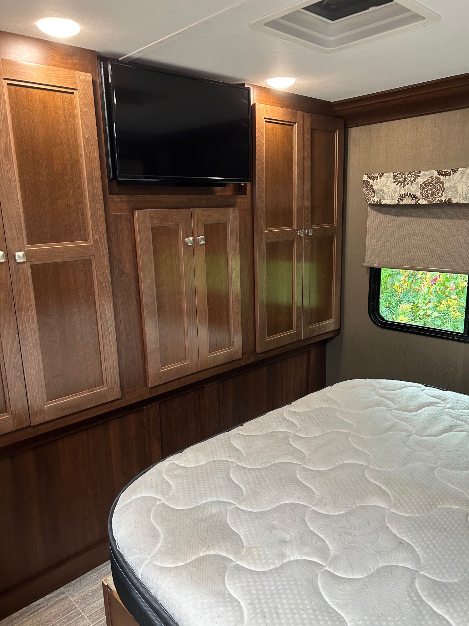 RV rental bedroom featuring a comfy bed, wall-mounted TV, wood cabinets, and window with outdoor view. Ideal for travel.. Forester Forester Motorhome 2020