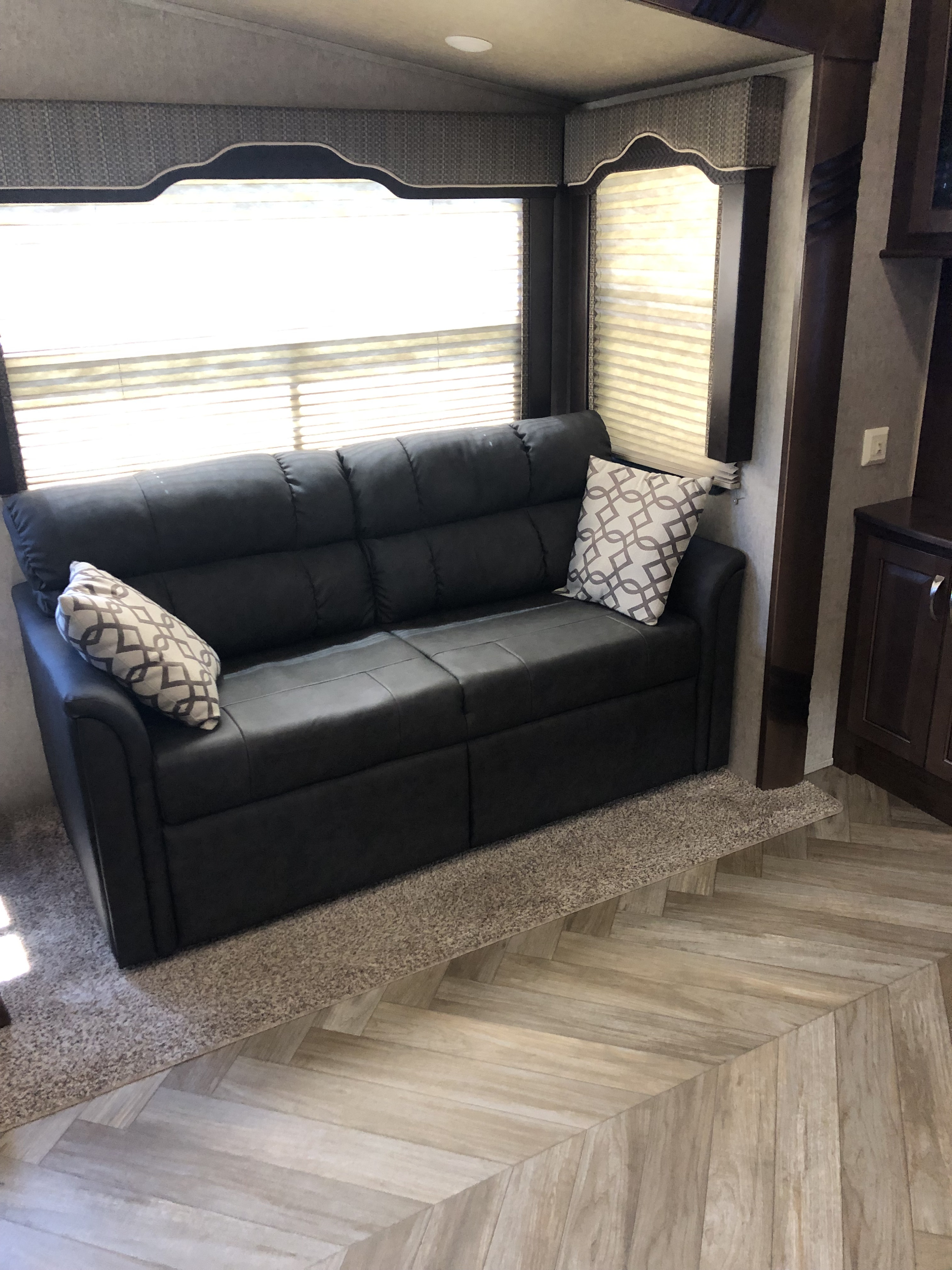 Comfortable RV rental living space featuring a modern sofa, windows with blinds, and herringbone flooring.. Forest River Other 2017