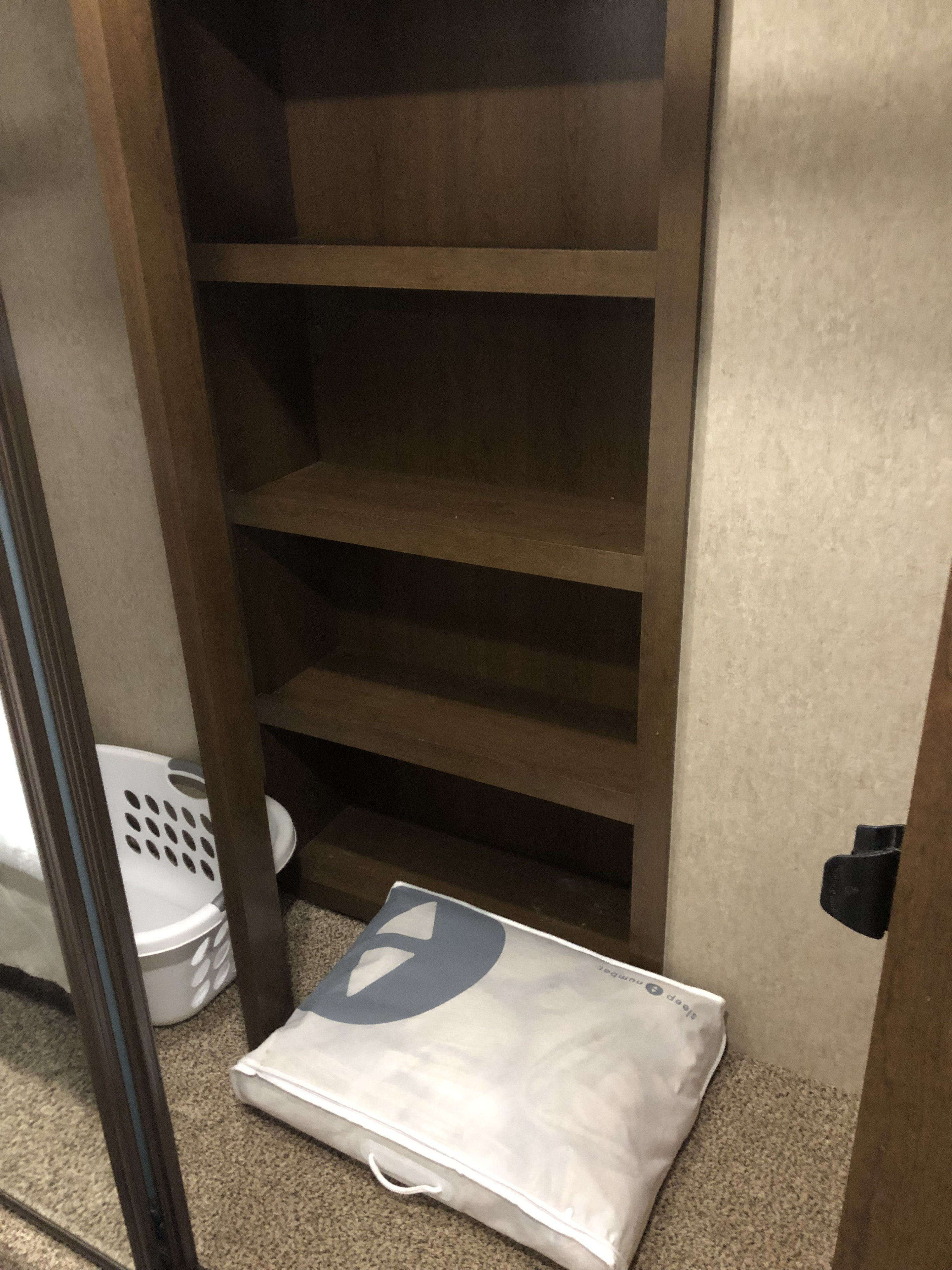 RV rental interior: empty built-in wooden shelves, a laundry basket, and a packaged pillow on the carpeted floor, ready for use.. Forest River Other 2017