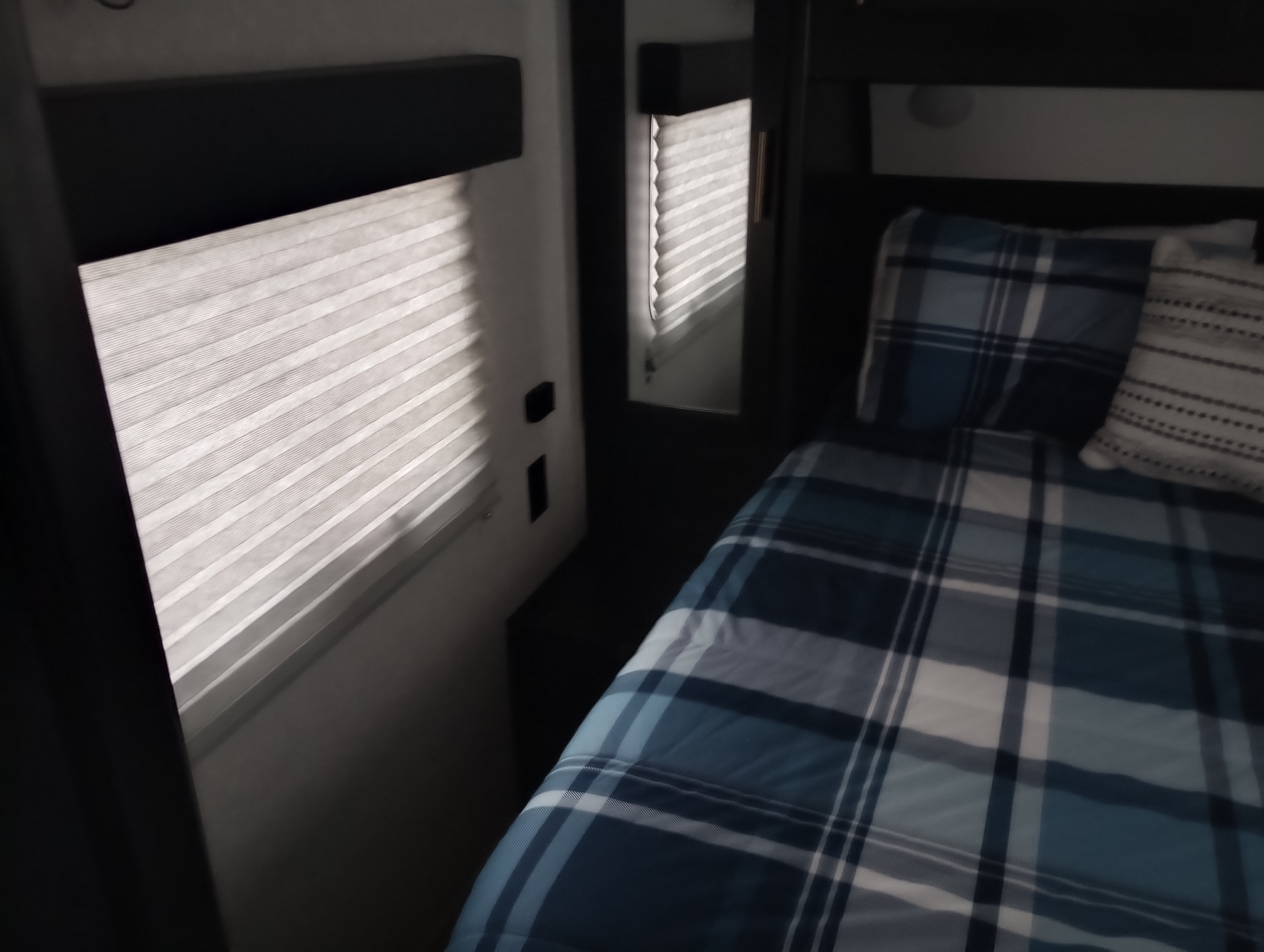Cozy RV rental bedroom featuring plaid bedding, bright window blinds, and a mirrored cabinet.. Forest River Cherokee 2022