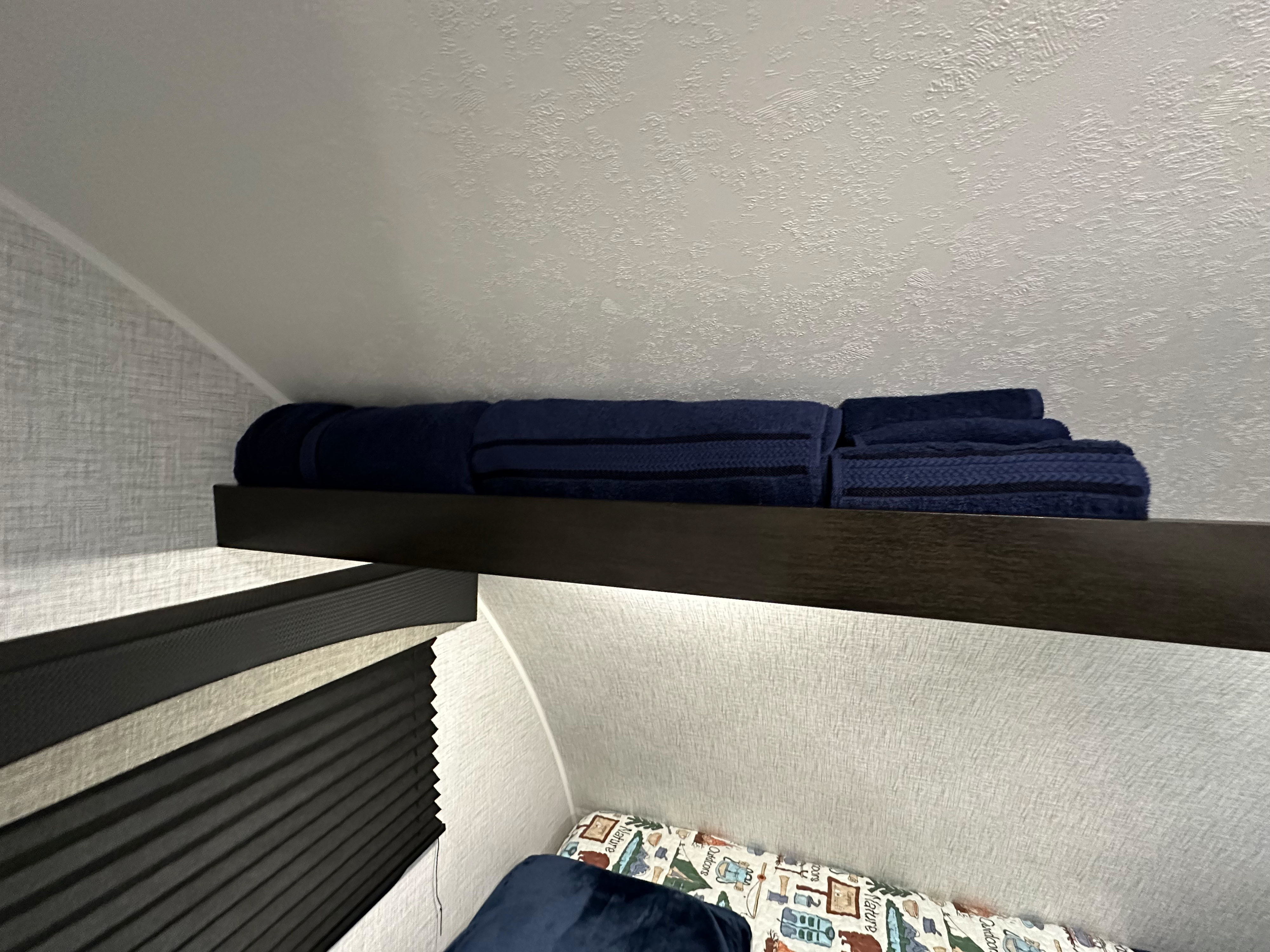 Cozy RV rental bunk area with a shelf of fresh blue towels, patterned bedding, and textured walls.. Braxton Creek Bushwhacker Plus 2023