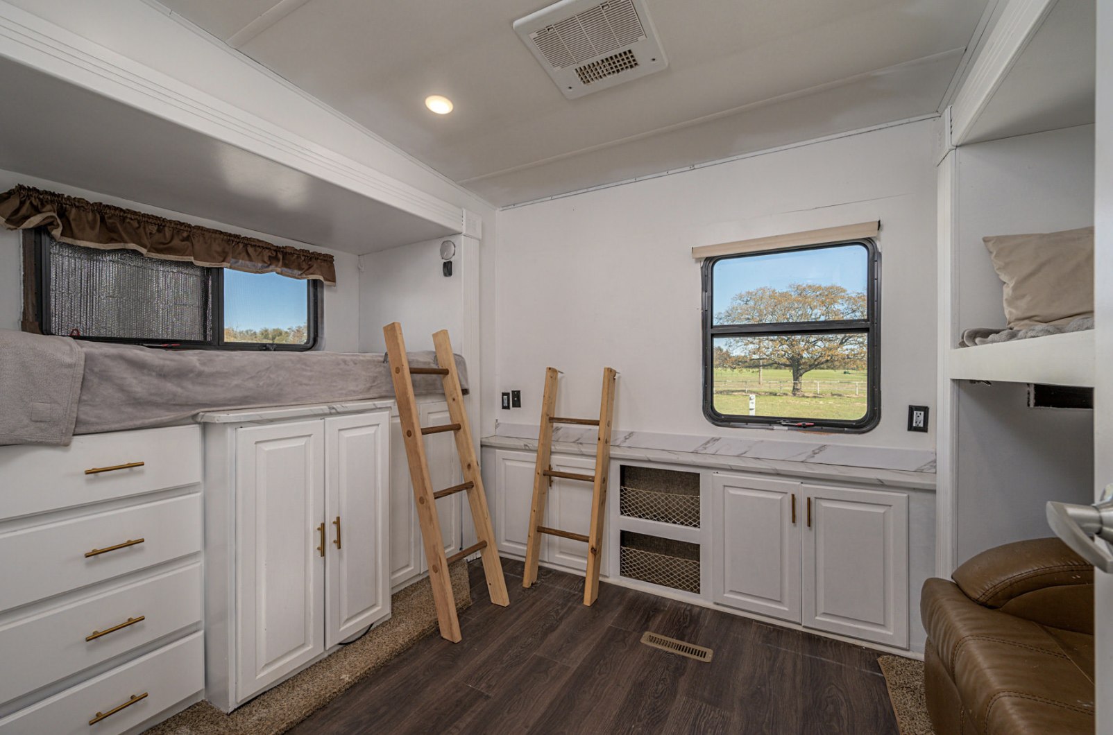 RV rental bunkhouse room with white cabinets, dark floors, and ladders to cozy bunks, offering outdoor views.. Heartland RVs Gateway 2016