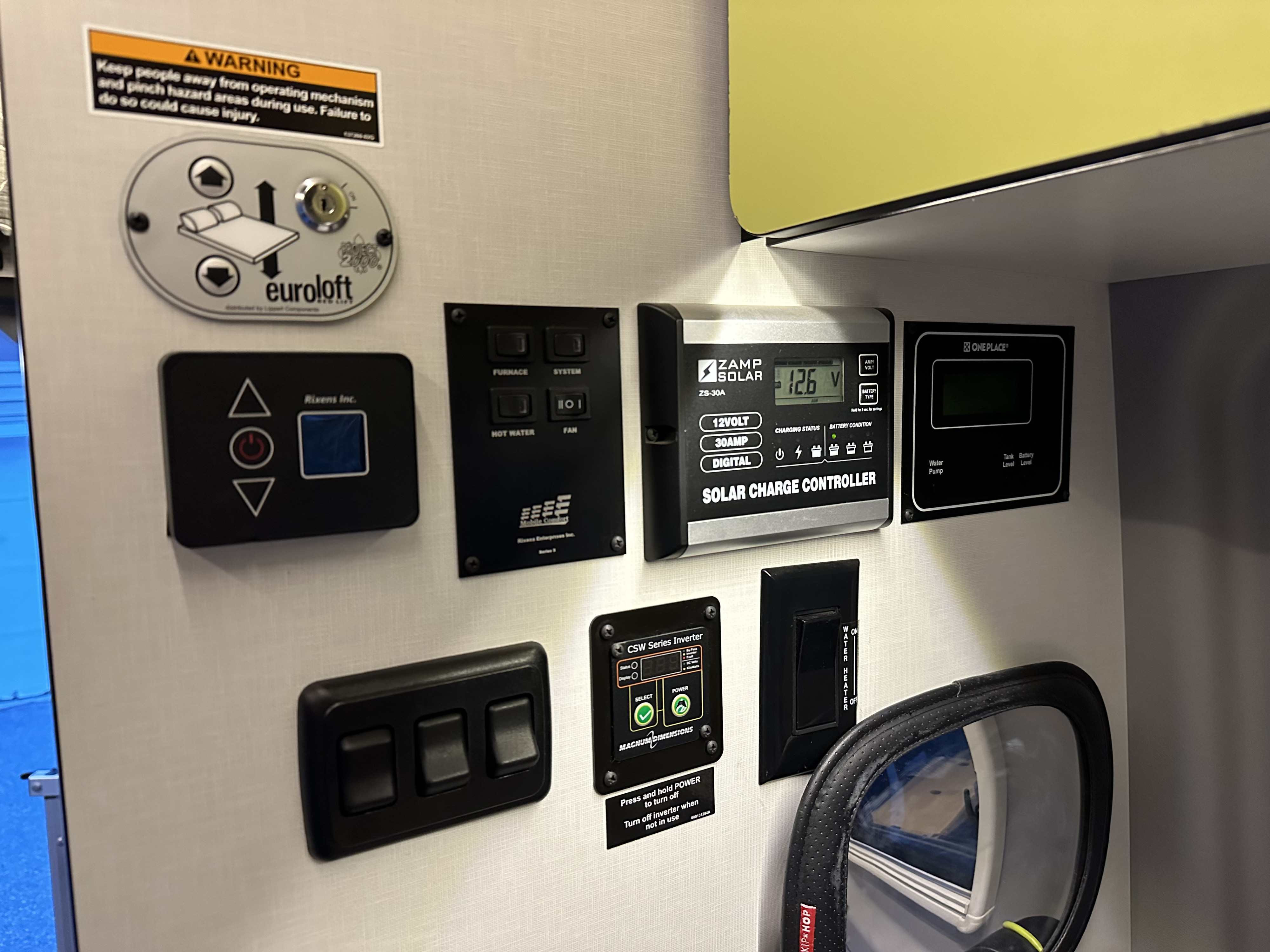 An RV rental's wall-mounted control center: Zamp Solar, OnePlace monitor, furnace, hot water, and a Eurolloft bed lift system.. Winnebago Revel 2020