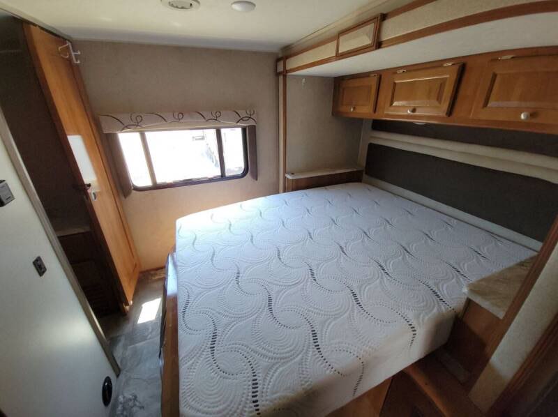 An RV rental bedroom showcasing a comfortable bed with a patterned mattress, overhead cabinets, and a side window.. Other Other 2019