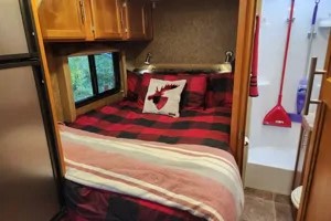 Cozy RV rental bedroom with red plaid bedding & moose pillow. Compact bath and fridge visible. Ideal for camping & travel adventures!. Adventurer Adventurer Motorhome 2017