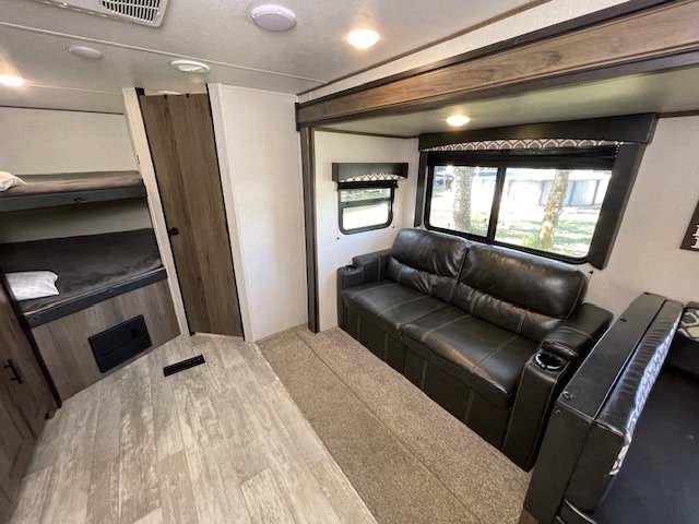 An RV rental's inviting interior: leather sofa, bunk beds, and wide windows showcasing outdoor views.. Avenger Avenger Trailer 2021