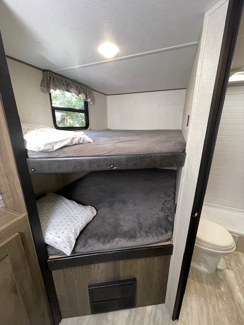 Cozy RV rental interior with comfortable bunk beds & a compact bathroom on the right. Perfect for family adventures.. Avenger Avenger Trailer 2021