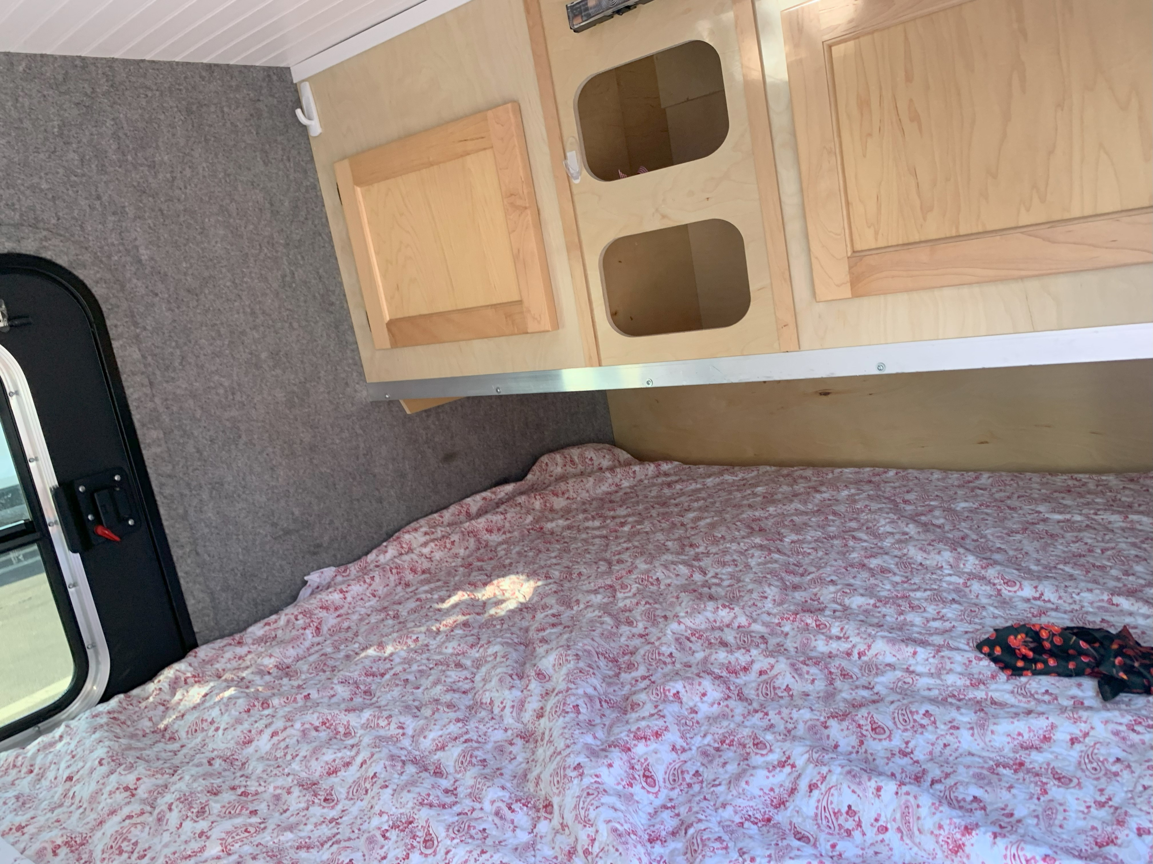 RV rental: Inside a compact camper, showing a red and white paisley bed, wood cabinets, and a side entrance.. American Merlin 2019