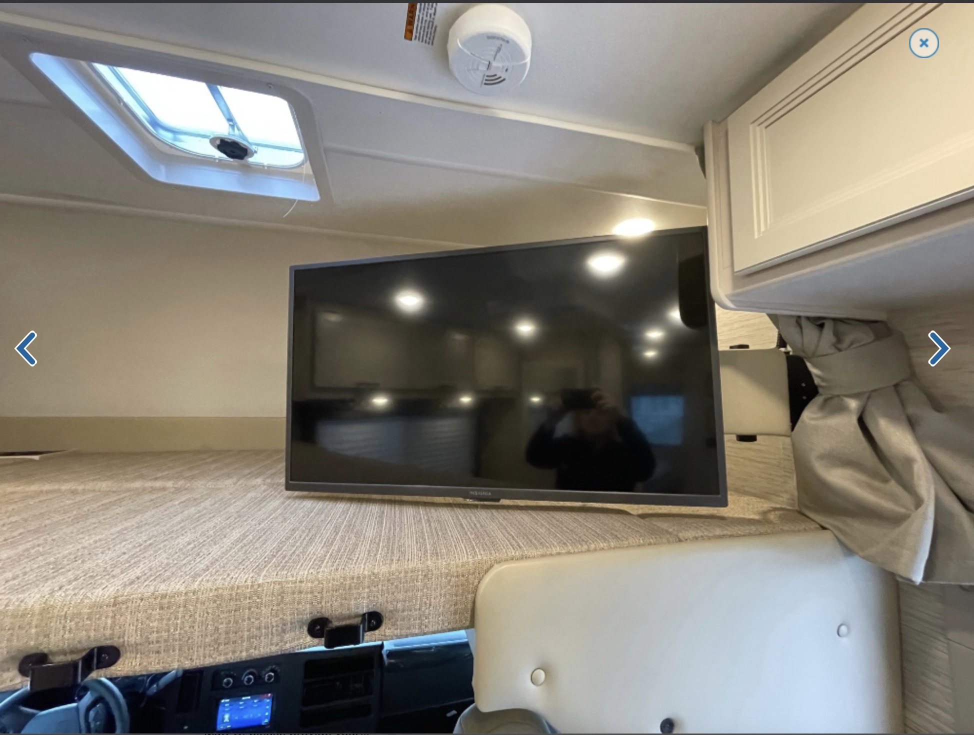 This RV rental features a cozy overhead bunk with a mounted TV, skylight, and dashboard view, offering a functional sleeping area.. Thor Freedom Elite 2023