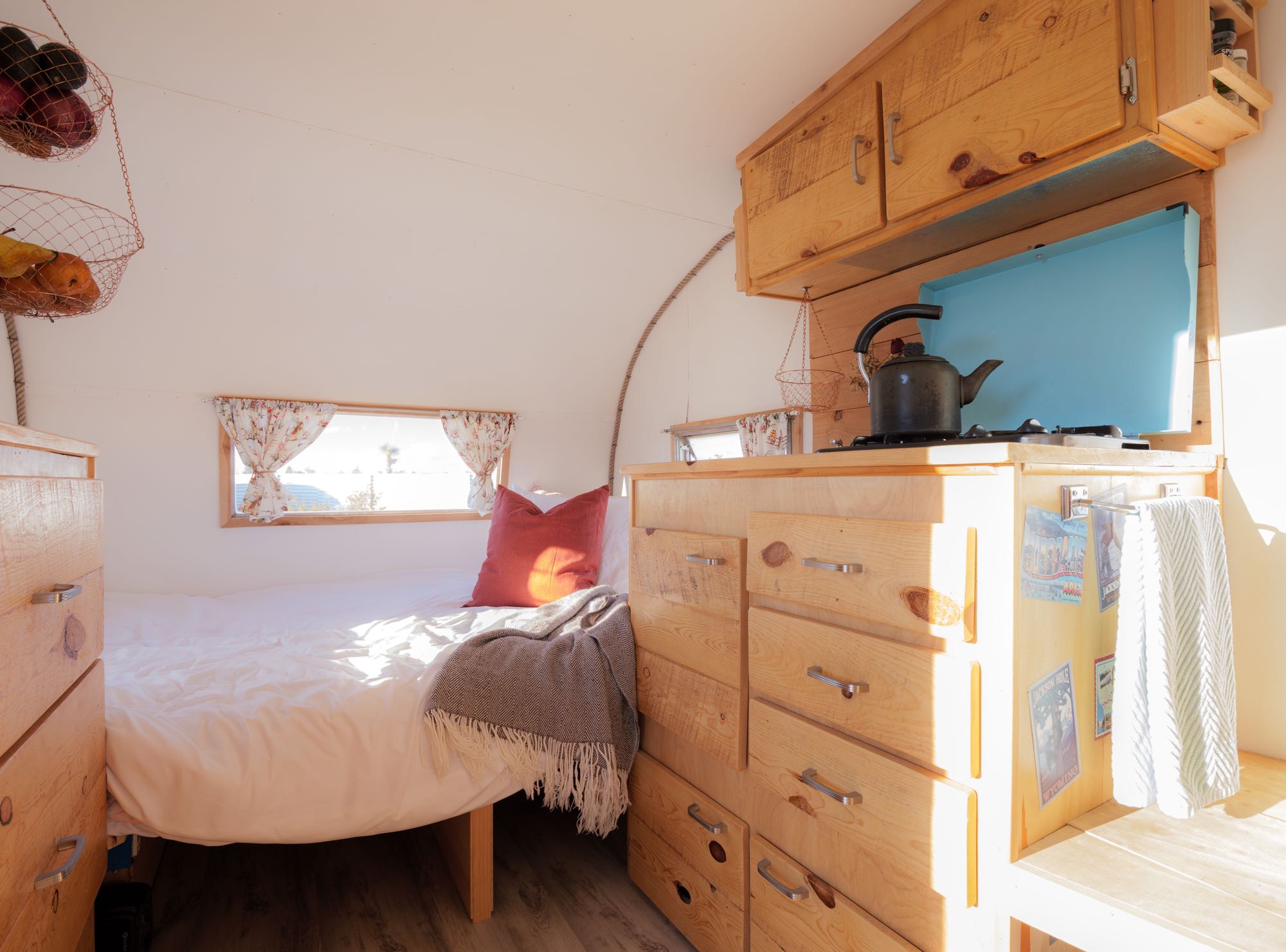 Cozy RV rental interior with bed, built-in wooden storage, and kitchen area. Bright and inviting.. Shasta Airflyte 1962