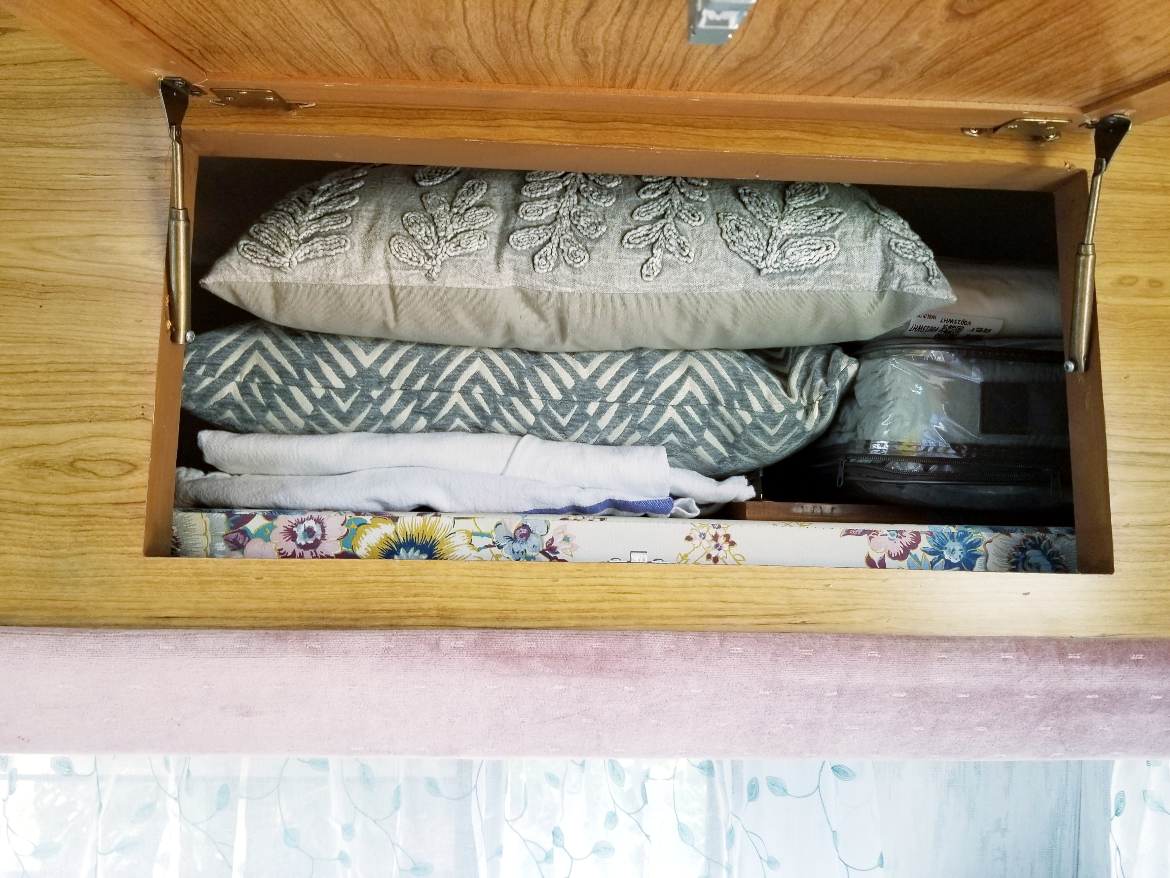 Organized RV rental overhead storage: decorative pillows, folded linens, and a floral-patterned item visible inside.. Fleetwood Prowler 1990