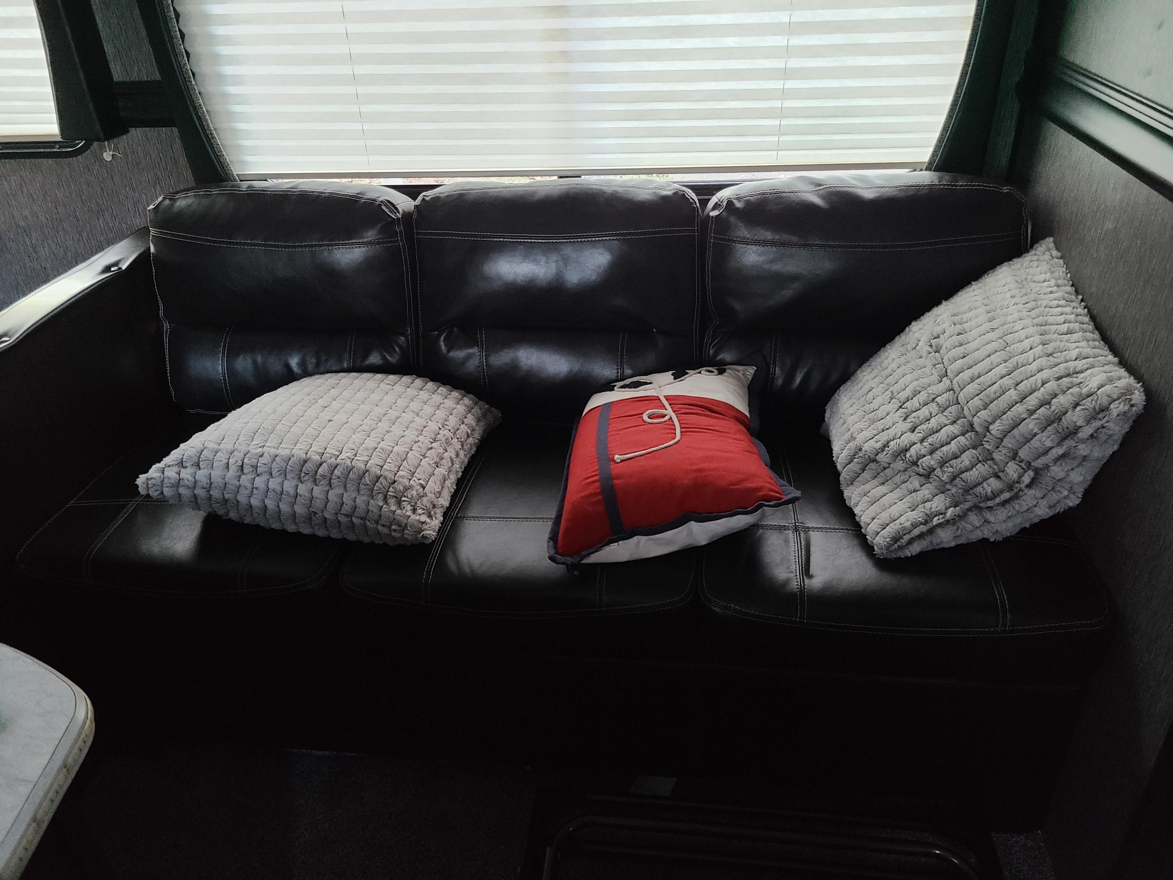 Cozy RV rental interior featuring a black leather couch, three comfy pillows, and window blinds.. Heartland RVs Pioneer 2019