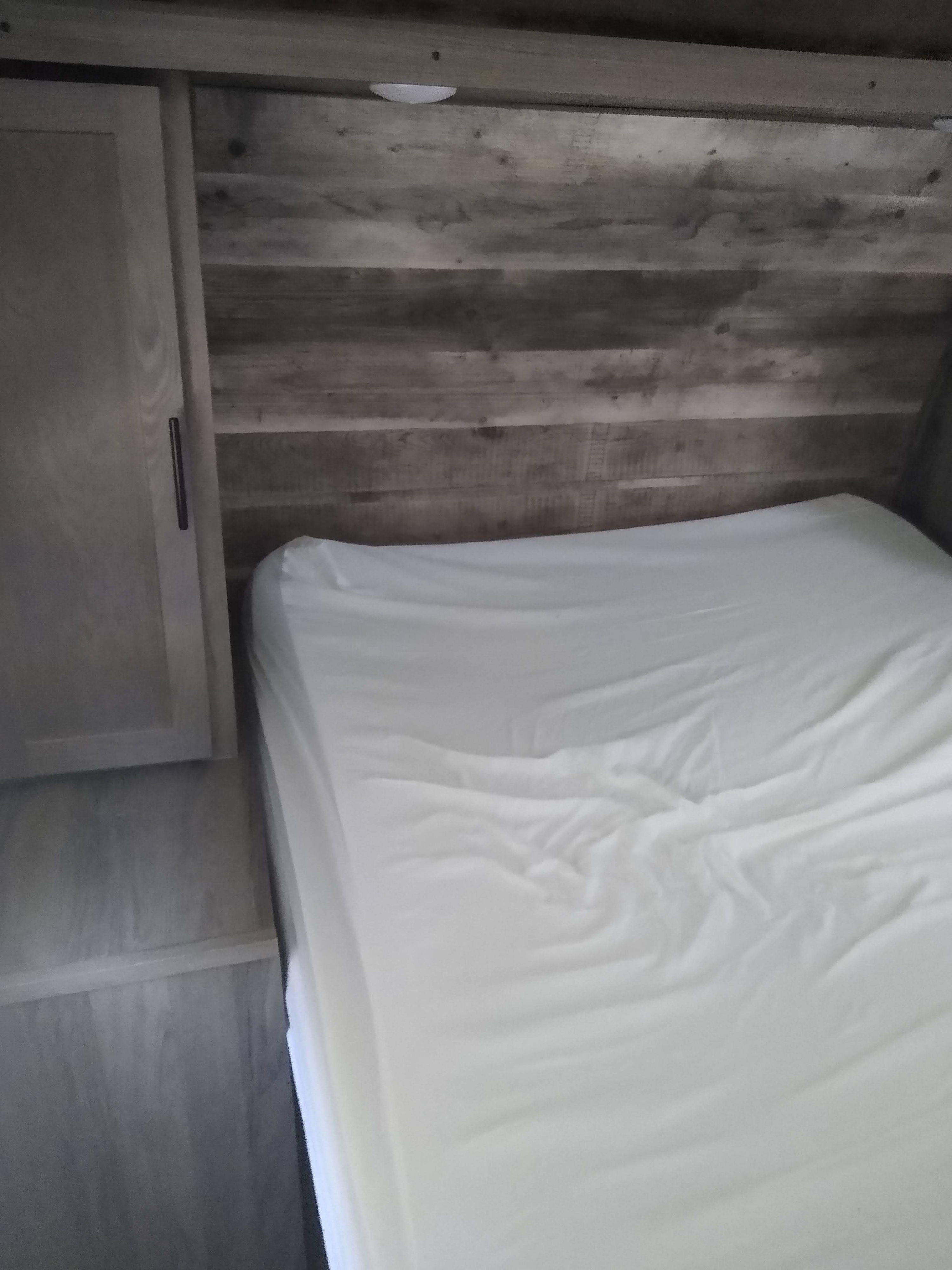 Relax in this RV rental bedroom: white bed, rustic wood walls, and convenient cabinet space.. Gulf Stream Kingsport 2021