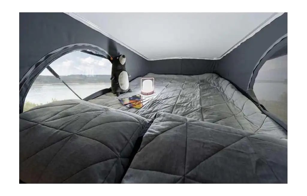 Relaxing RV rental interior: soft bed, reading lamp, and beautiful waterside view from this pop-top camper.. Winnebago Solis 2023