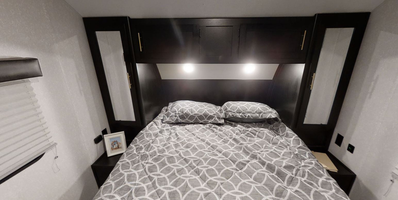 Cozy RV rental bedroom with a full bed, overhead storage, and built-in lighting. Textured walls and modern dark cabinetry create a comfortable space.. Forest River Cherokee Grey Wolf 2022