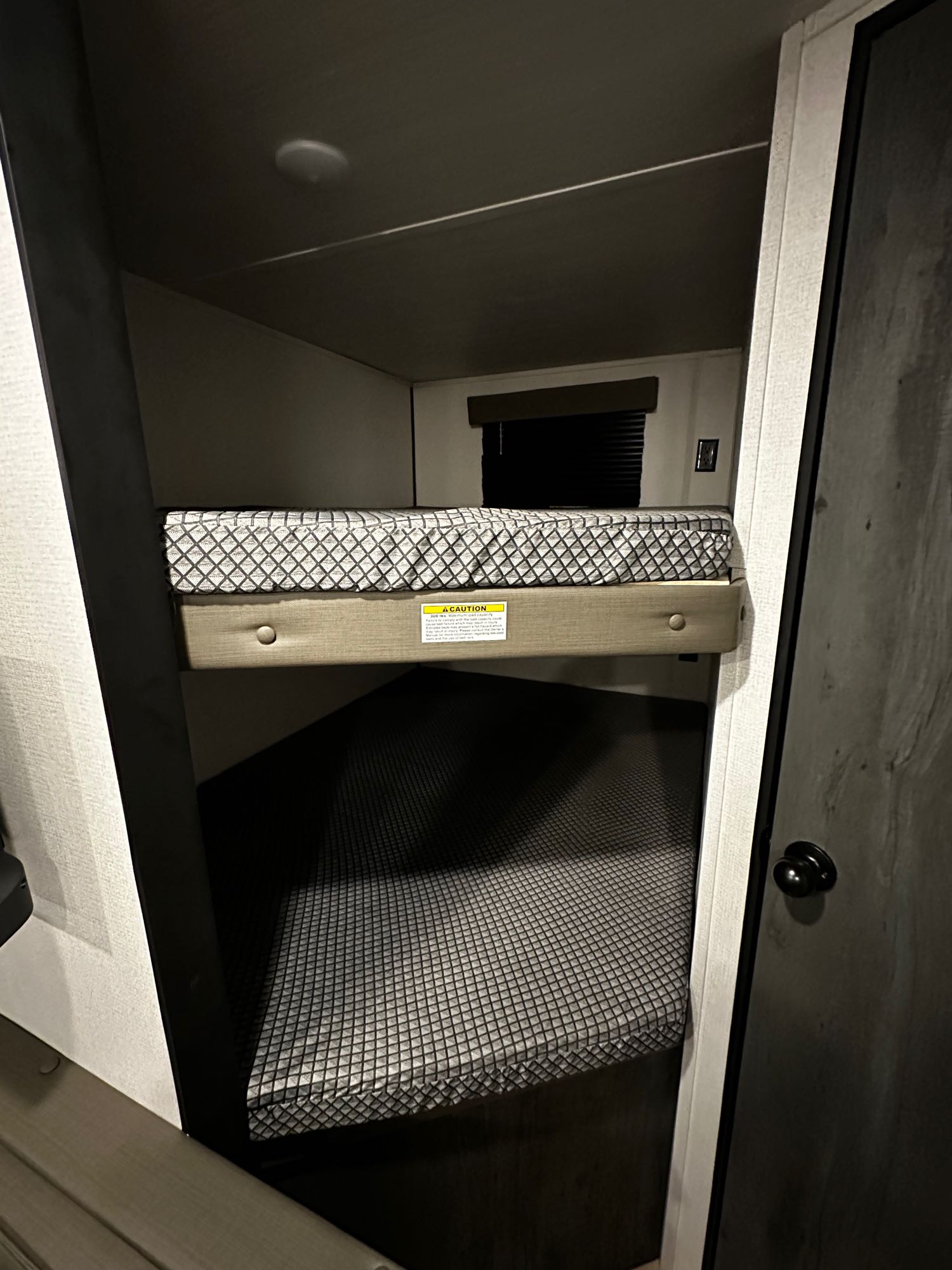 Two cozy bunk beds in an RV rental, featuring patterned mattresses and a window blind. Ideal for family adventures.. Keystone RV Hideout 2022