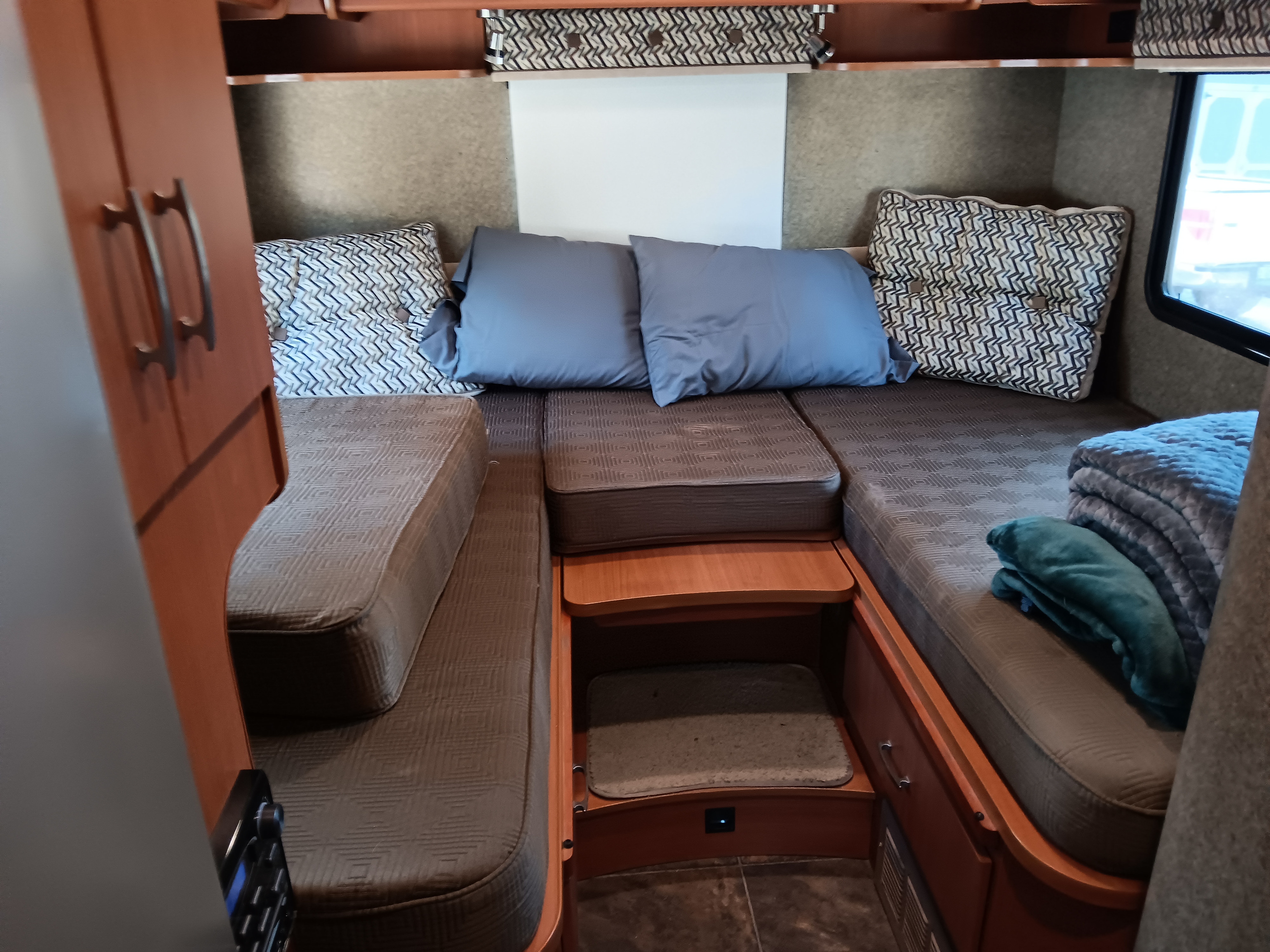 RV rental sleeping area: Cozy beds with patterned cushions, blue pillows, and built-in steps/storage.. Itasca Navion 2013
