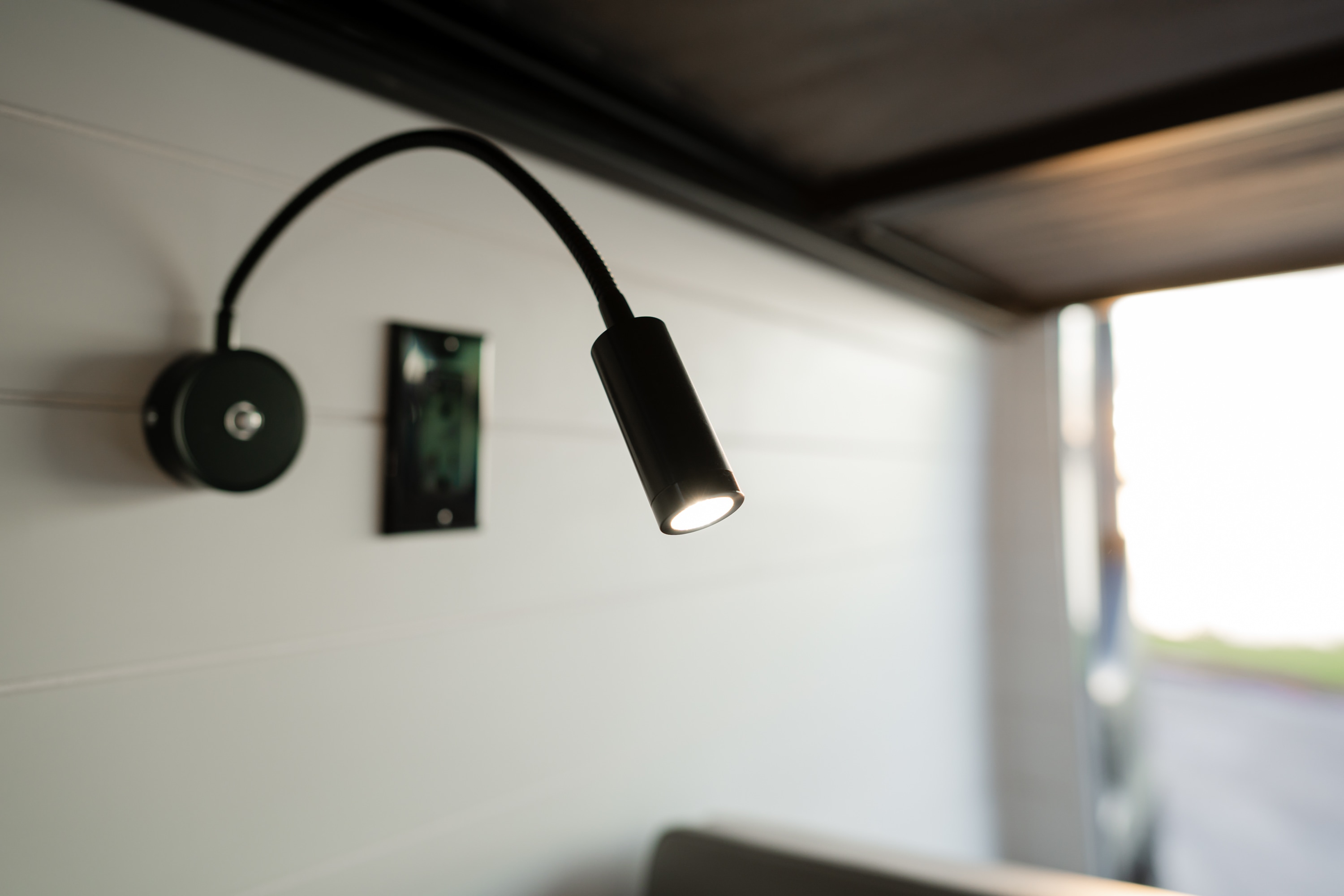 Illuminated black gooseneck LED light mounted on a white plank wall, characteristic of a modern RV rental interior.. Mercedes-Benz Sprinter 2022
