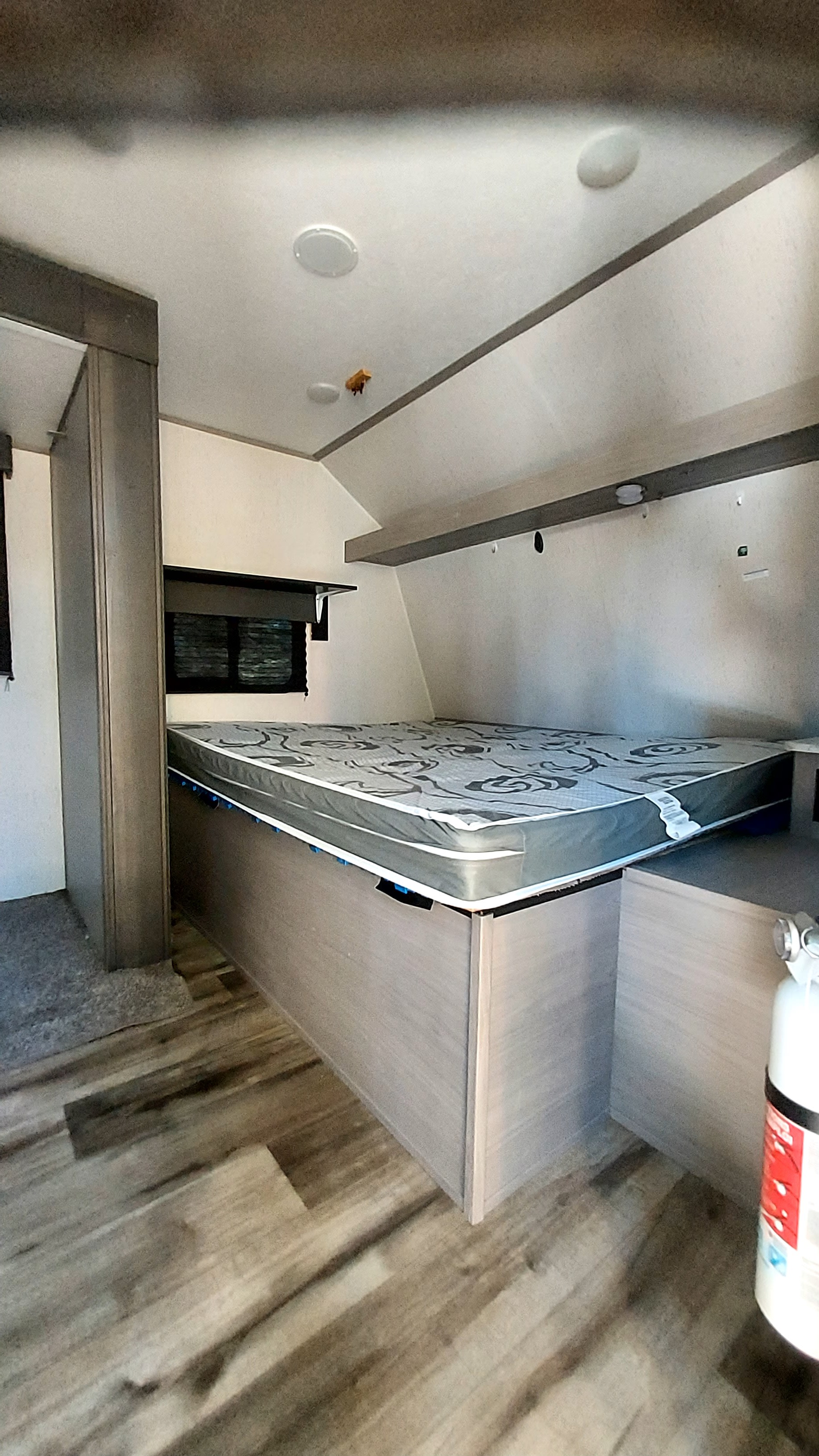 Inside an RV rental: a cozy bedroom with patterned mattress, built-in storage, wood-look floor, and ceiling lights.. Dutchmen Coleman Lantern LT 2023