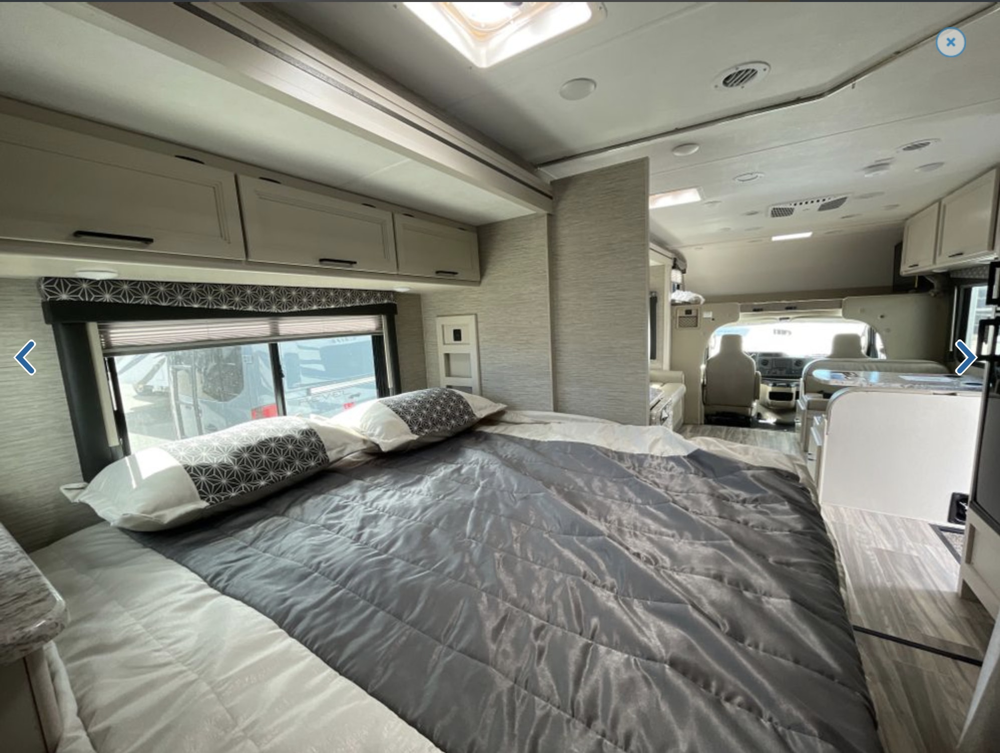 Spacious RV rental interior: Bedroom with gray comforter, flowing into the living area and cockpit.. Thor Freedom Elite 2023