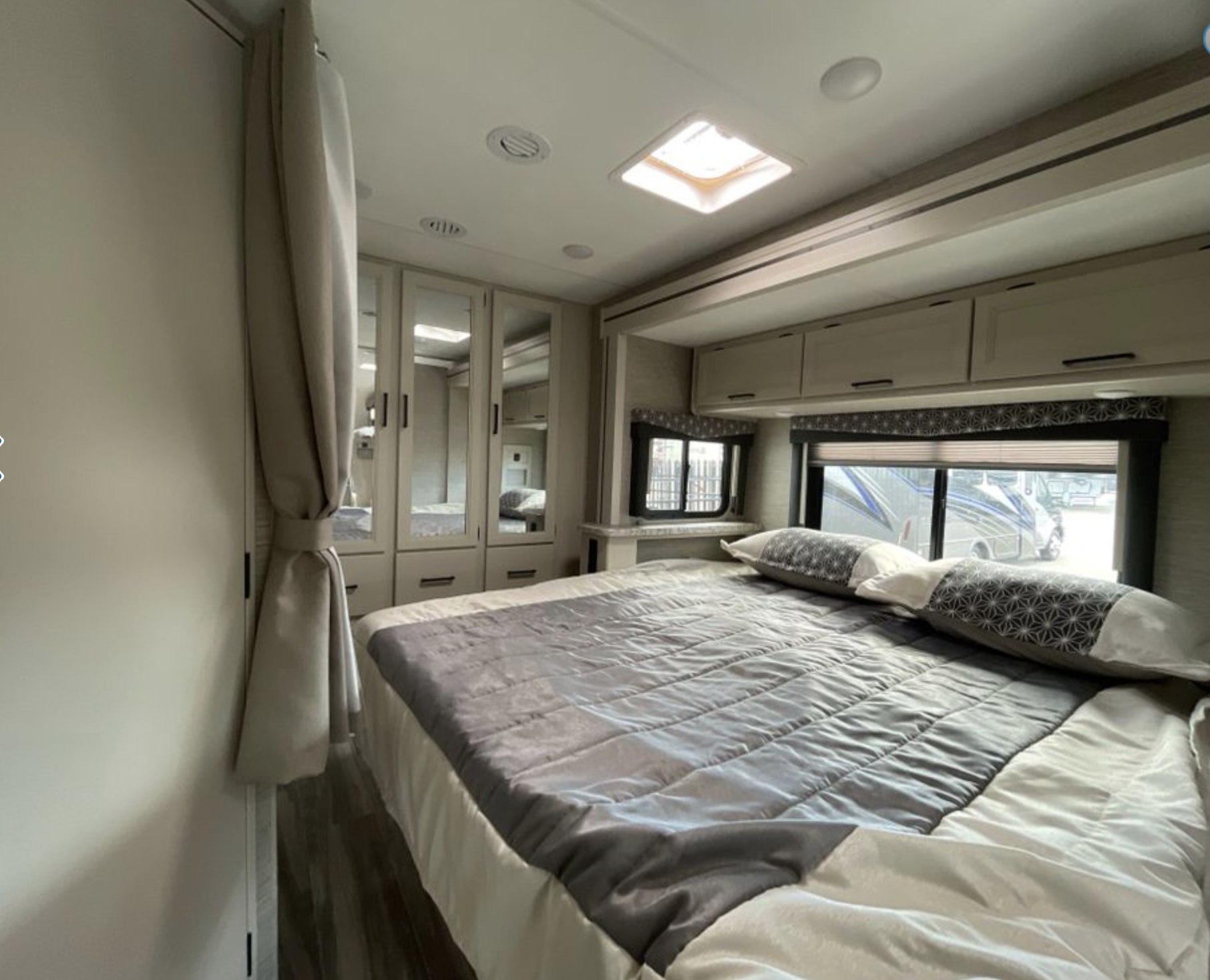 Modern RV rental bedroom: A comfortable bed with grey/white bedding, mirrored wardrobes, and overhead cabinets for cozy travels.. Thor Freedom Elite 2023