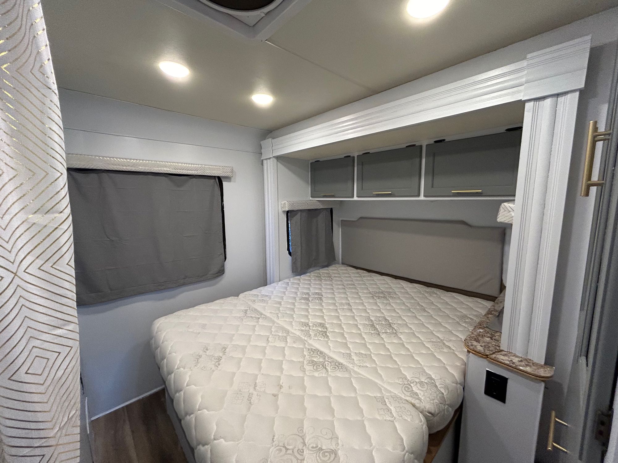 Well-lit RV rental bedroom with a large bed, overhead storage, and stylish grey and gold accents.. Thor Four Winds 2017