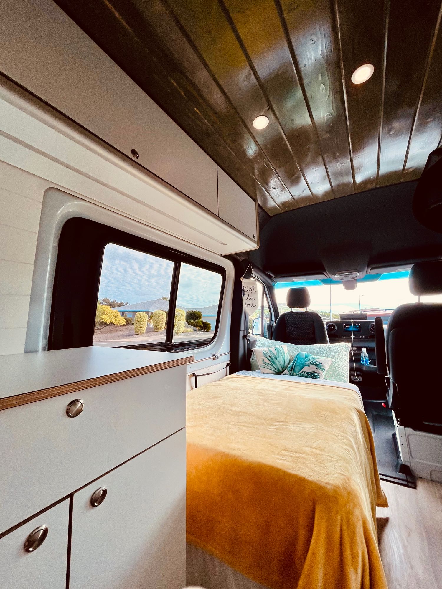 Cozy RV rental interior with a comfortable bed, wooden ceiling, modern cabinets, and a window showcasing a scenic view.. Mercedes-Benz 2500 Cargo 170 2023