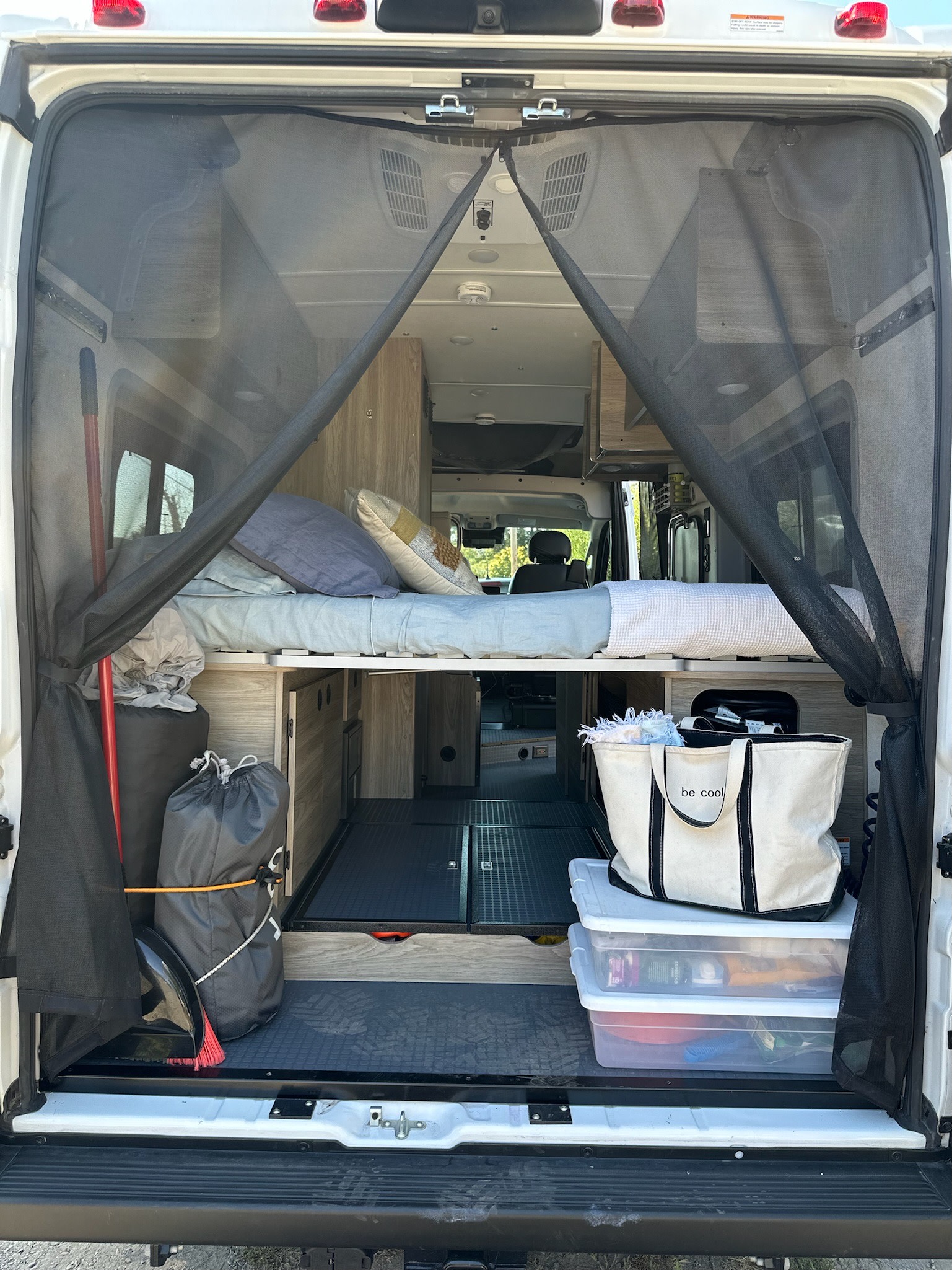 RV rental van interior seen from the rear: a raised bed, modular storage, and a black mesh bug screen for airflow.. Winnebago Solis 2023