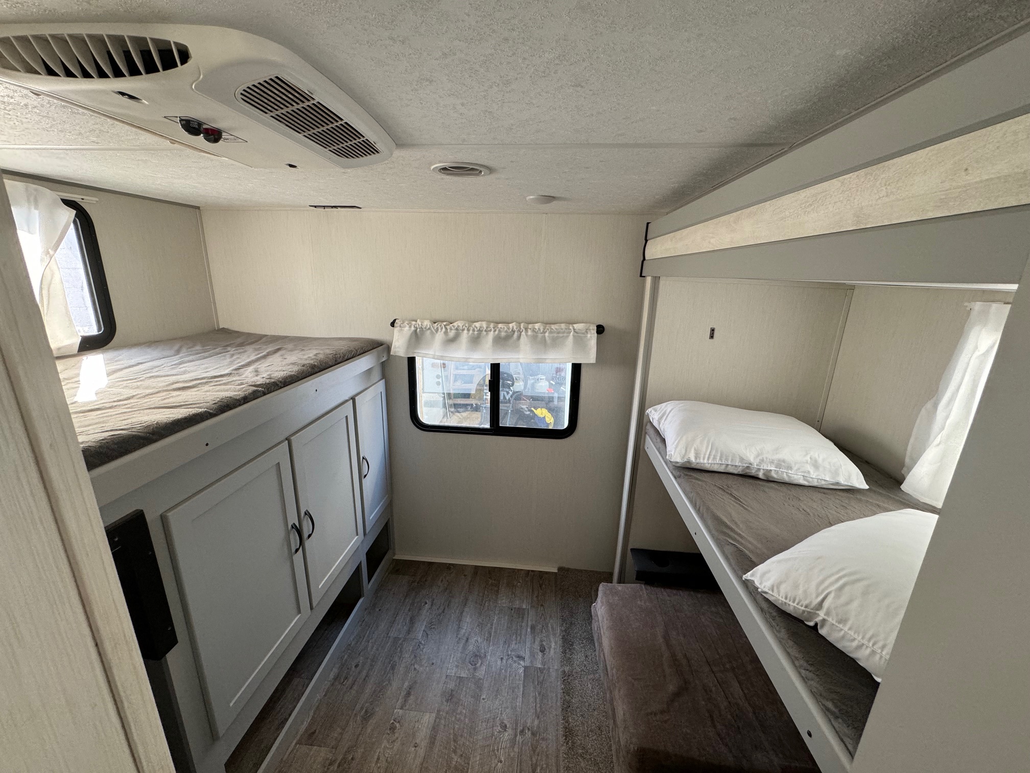 Inside an RV rental: a comfortable sleeping area with two sets of bunk beds, storage, and an AC unit.. Forest River Vibe 2021