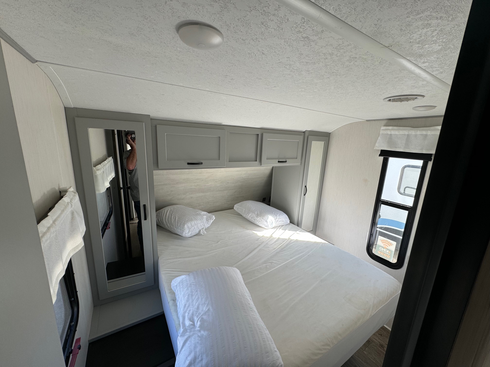 Inside an RV rental: a modern bedroom with white bedding, gray cabinets, dual mirrors, and ceiling AC vent.. Forest River Vibe 2021