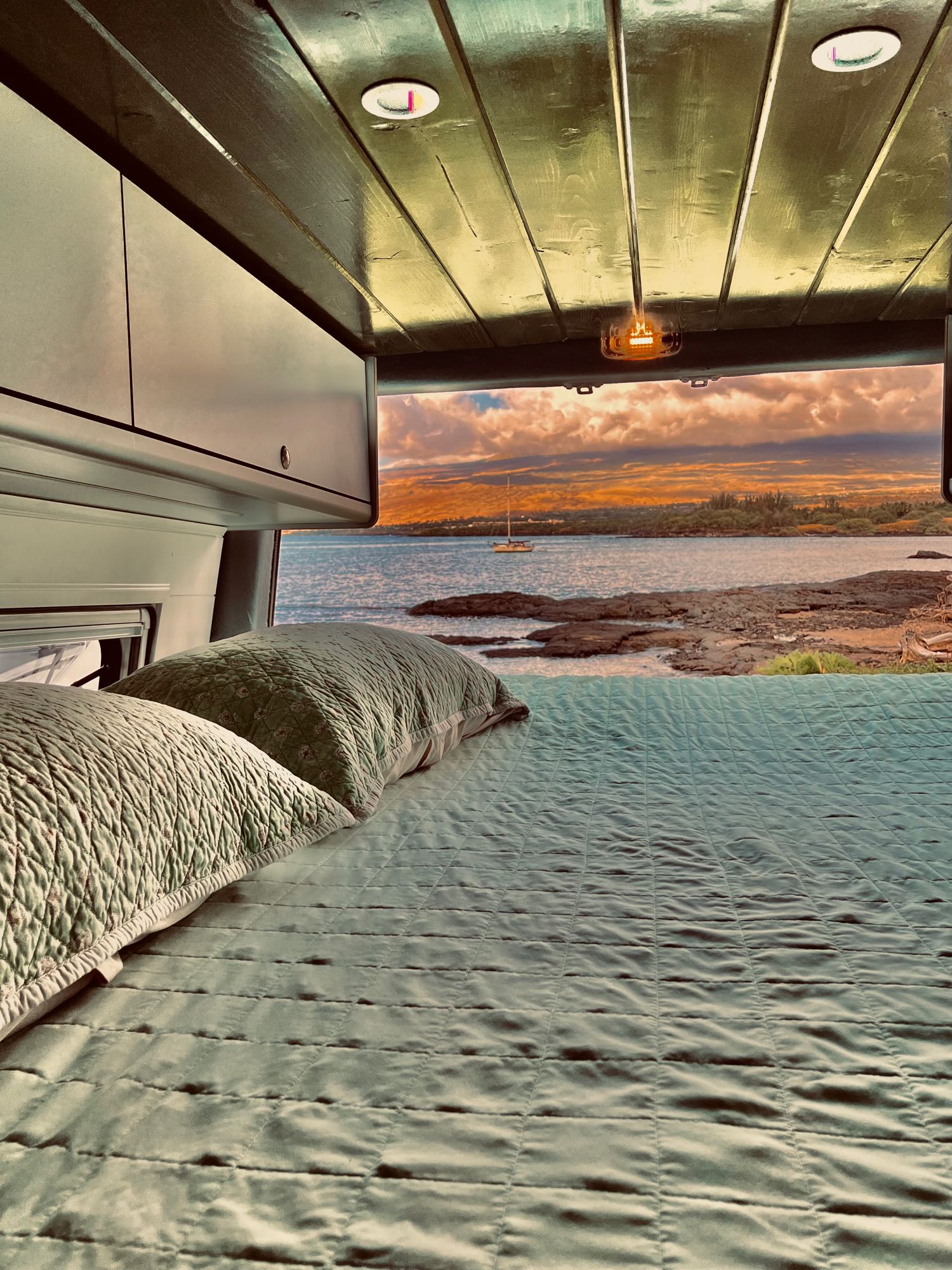 Wake up to paradise! This cozy RV rental features a comfortable bed overlooking a stunning ocean sunset with a distant sailboat.. Mercedes-Benz 2500 Cargo 170 2023