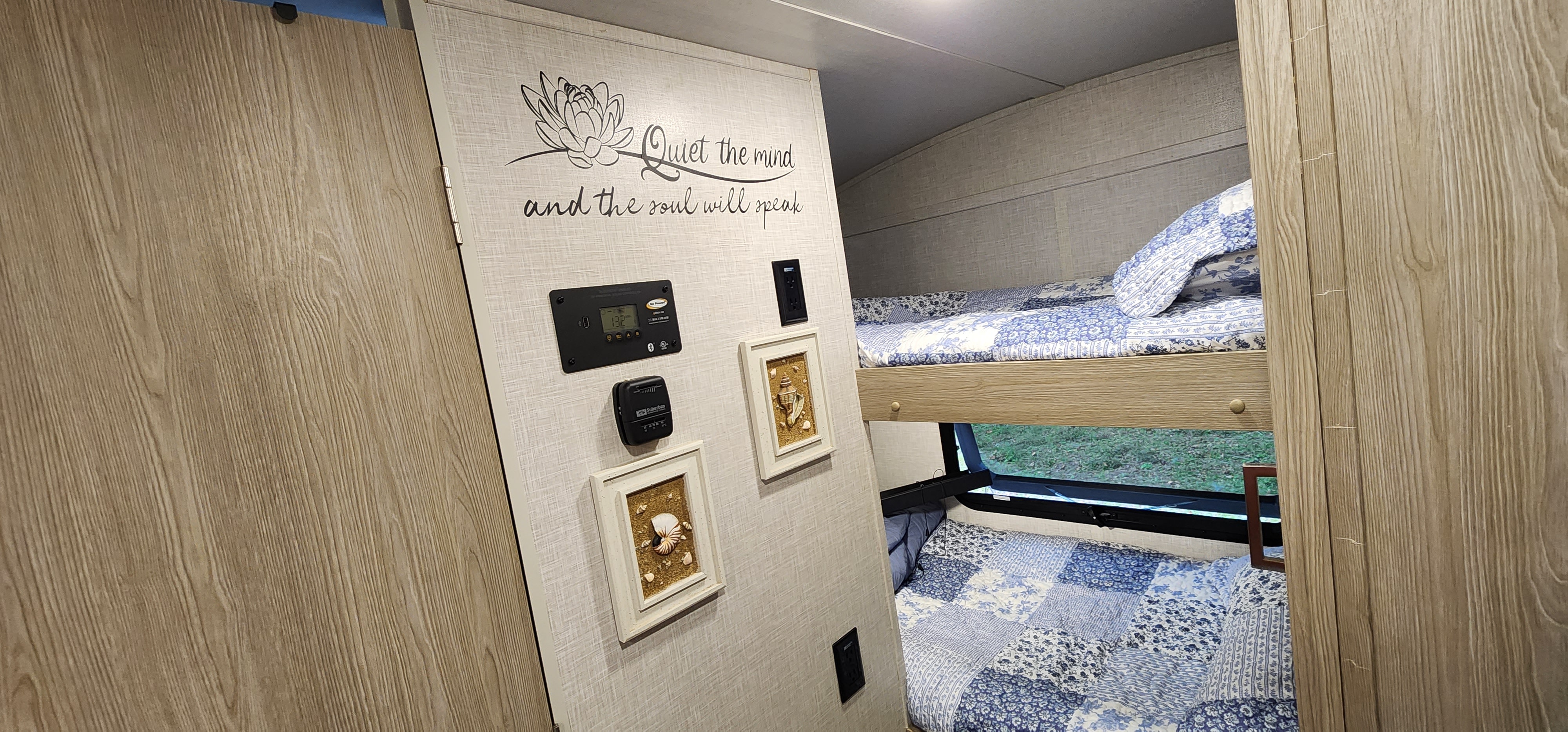 Cozy RV rental interior: bunk beds with blue quilts, "Quiet the mind" wall decor, and control panels.. Forest River Rockwood Geo Pro 2021