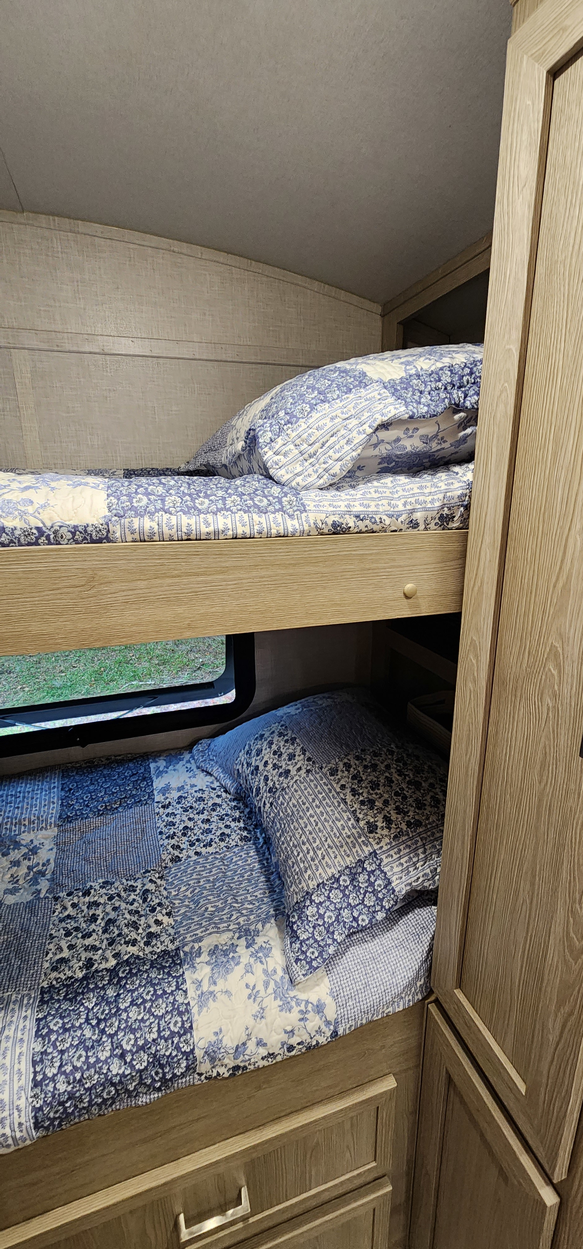Cozy bunk beds in an RV rental, featuring blue and white patterned bedding. A window next to the lower bunk offers a glimpse of nature.. Forest River Rockwood Geo Pro 2021